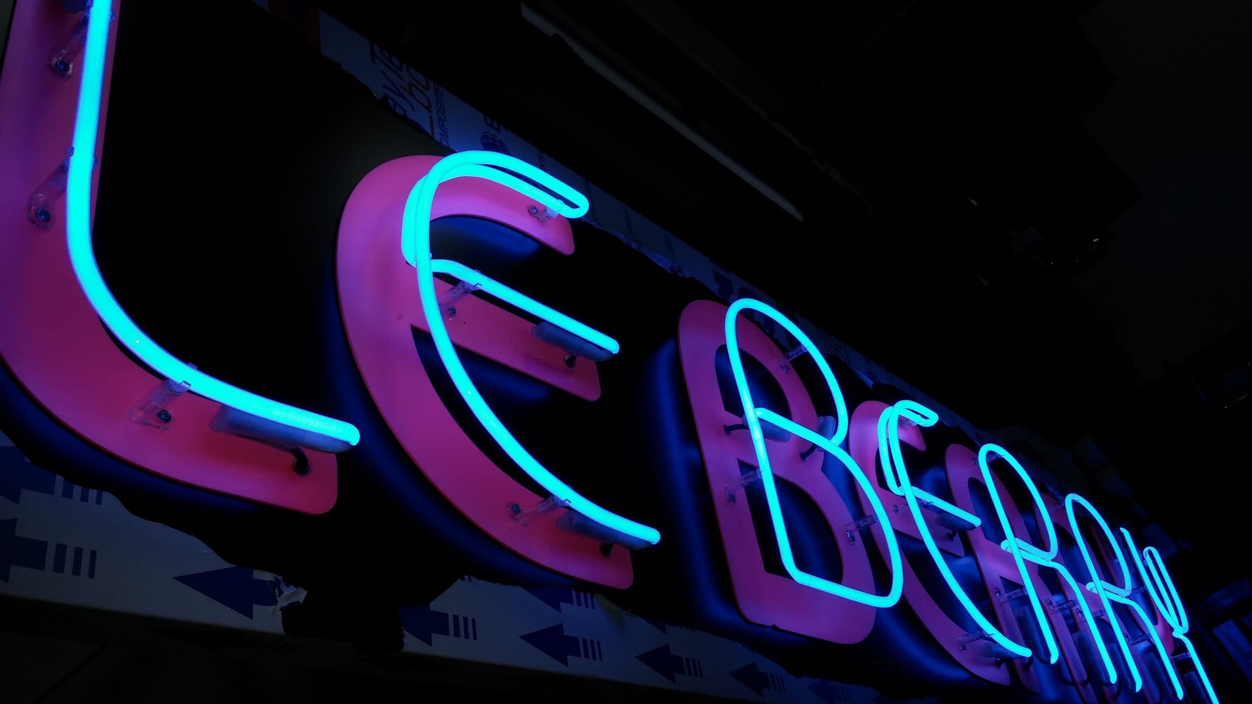 Близък план на светещи сини тръби, оформящи букви, монтирани върху розова основа в пълна тъмнина.