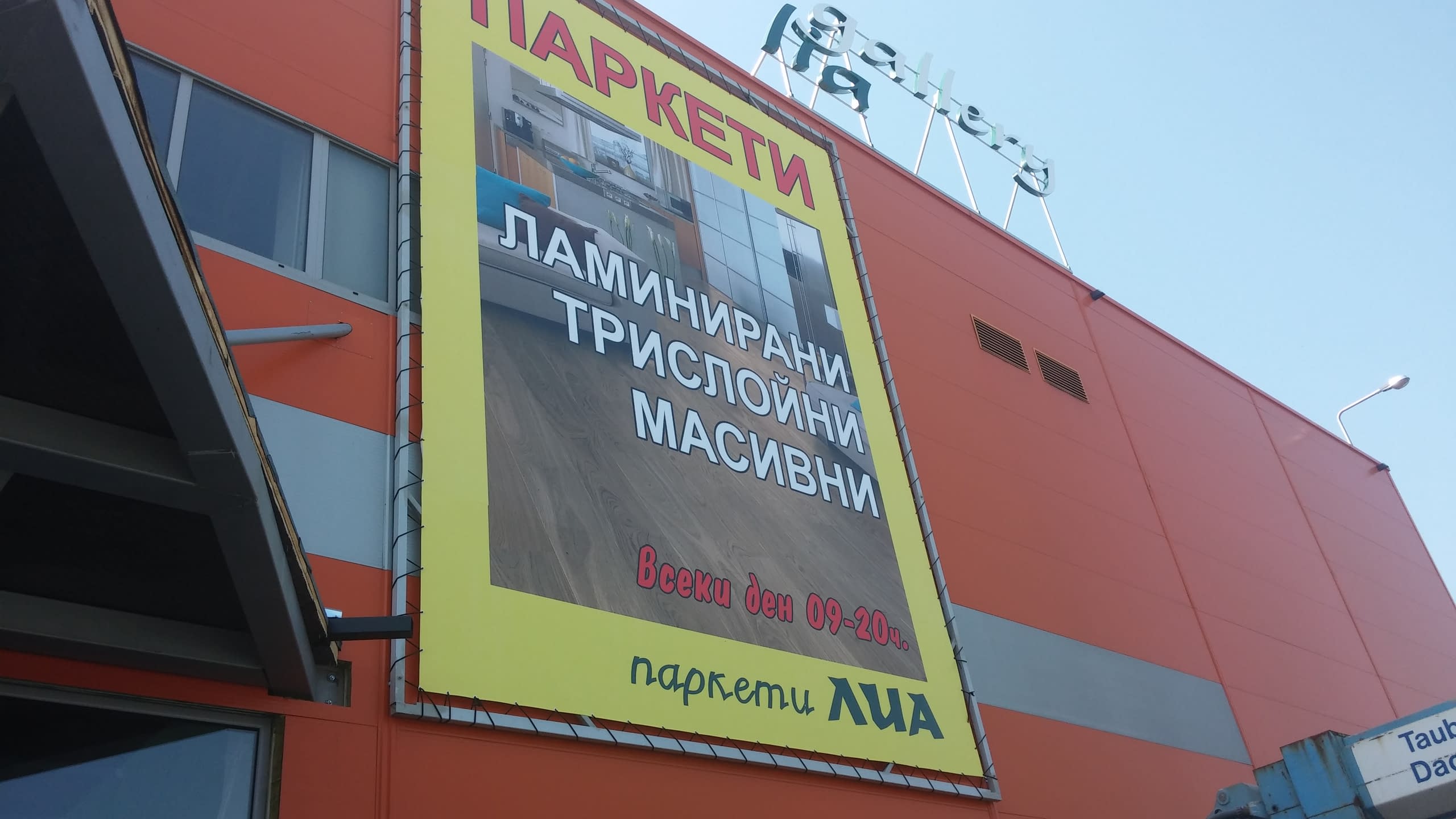Голям жълт винилов банер за паркети, монтиран на оранжева сграда, с изброени видове настилки.