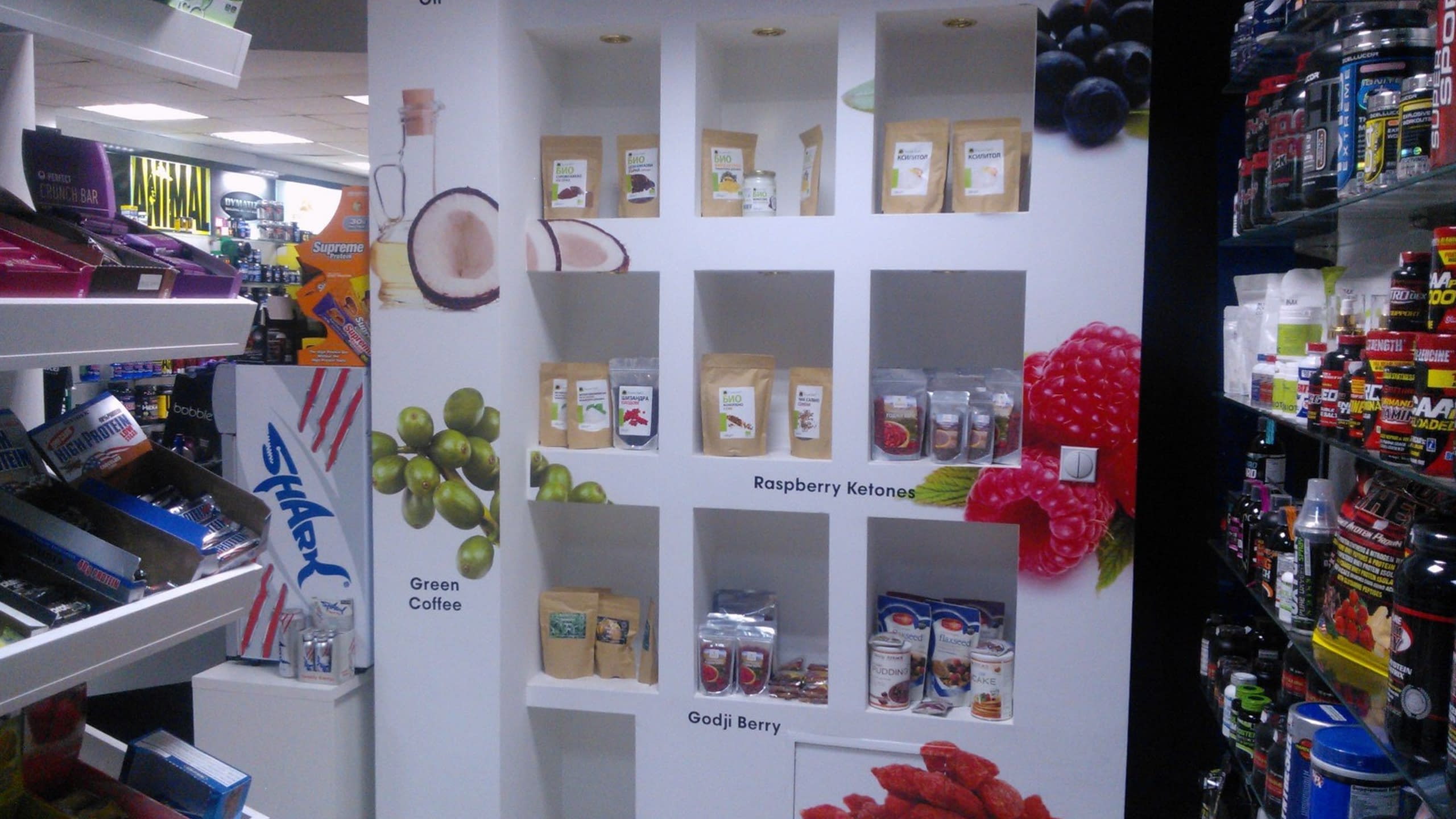 Стелаж в магазин със специално обособени ниши, декорирани с големи изображения на кокос, зелено кафе, малини и други плодове.