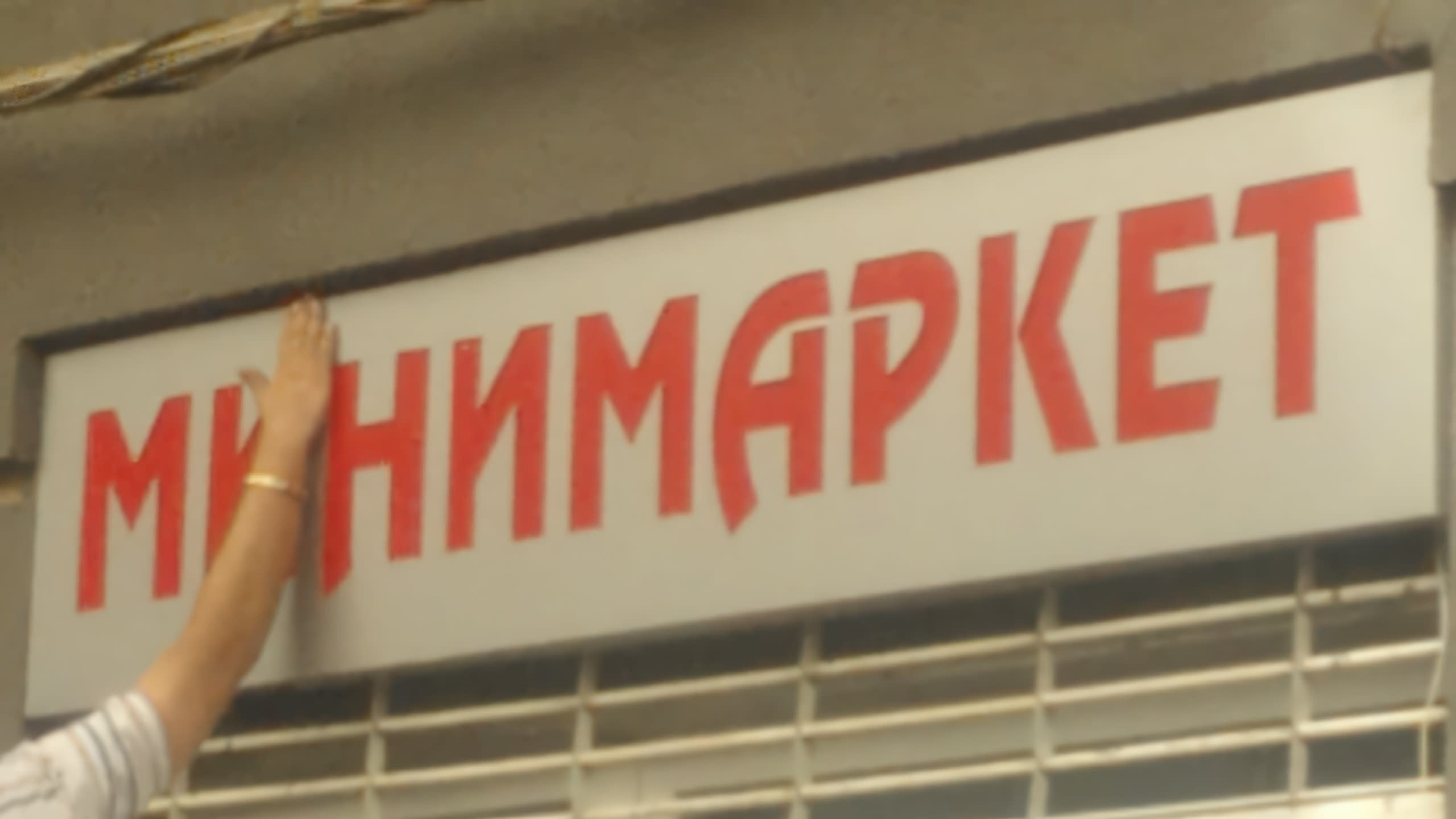 Ръка, която монтира светеща табела с надпис "Минимаркет" на стената на сграда.