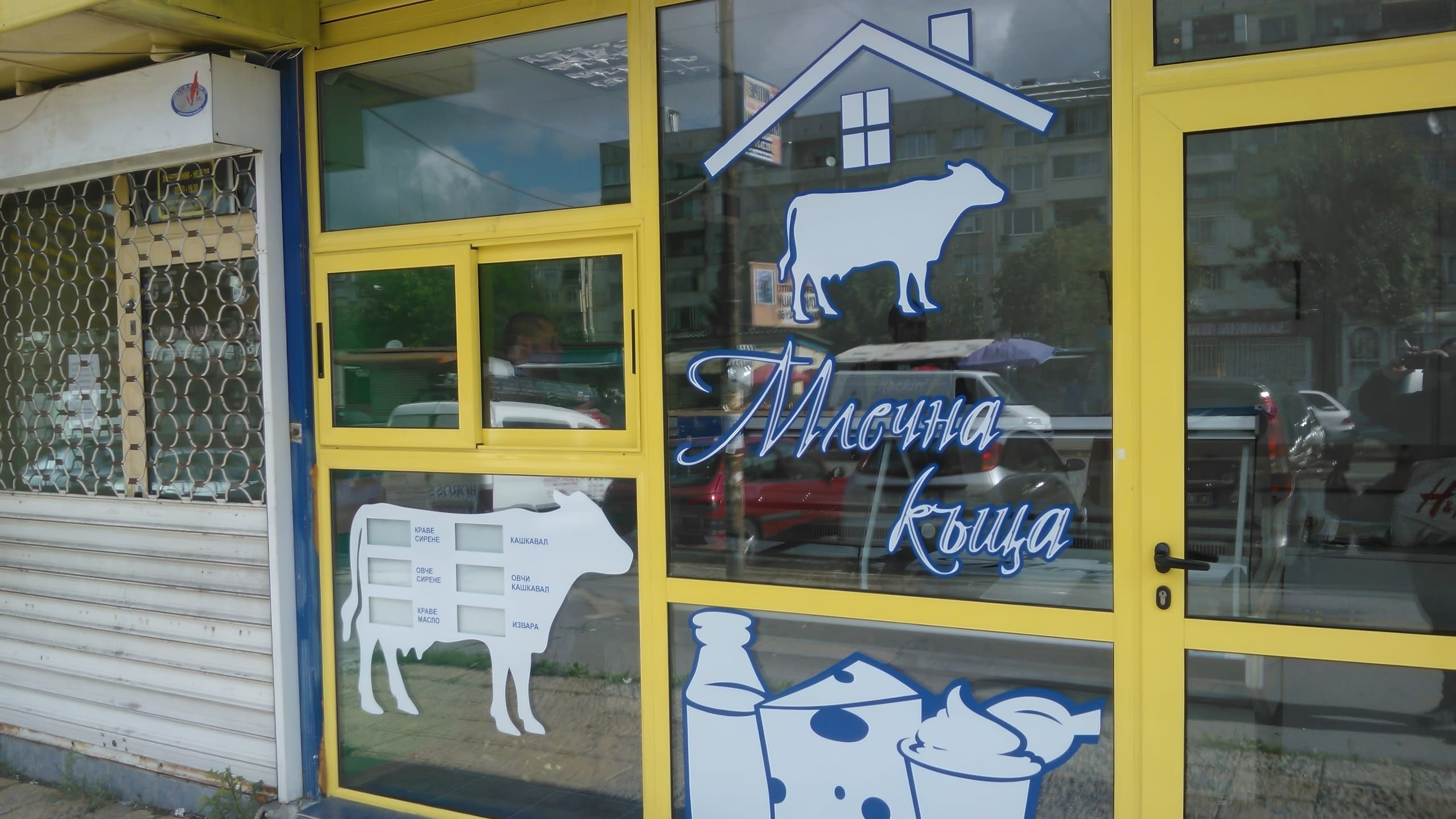 Надписи и графики от бяло и синьо фолио на витрината на магазин за млечни продукти.