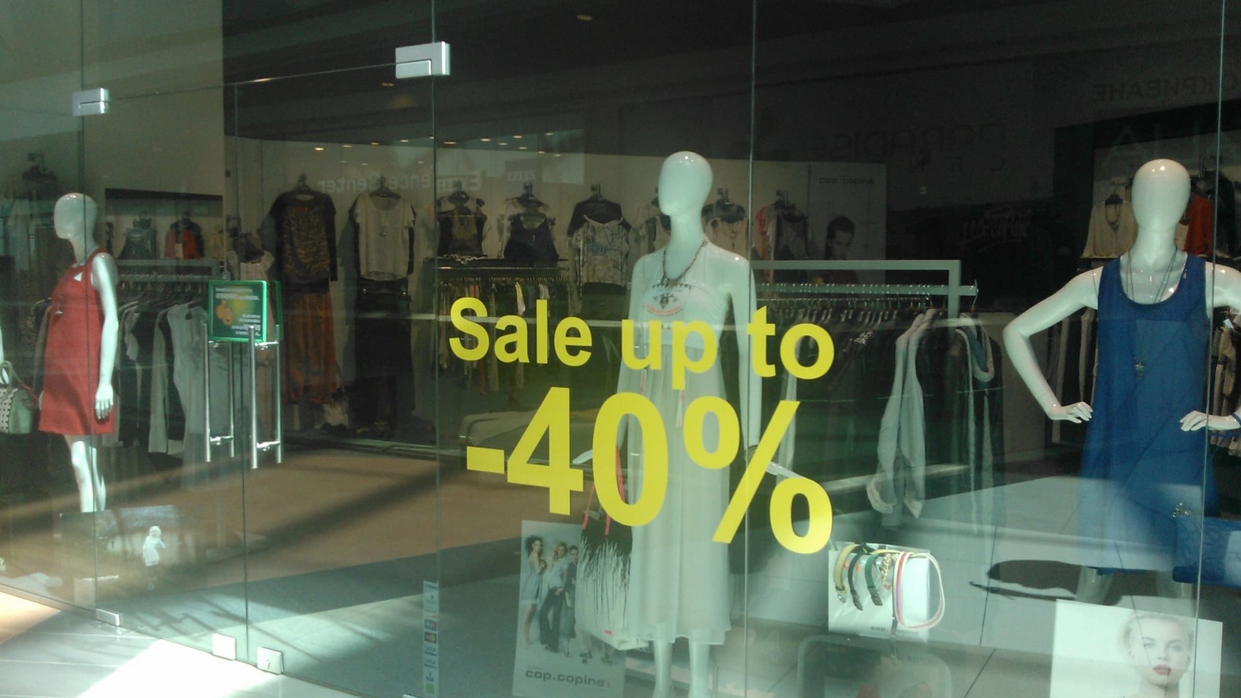 Витрина на магазин за дрехи с жълт надпис от фолио 'Sale up to -40%' и манекени.