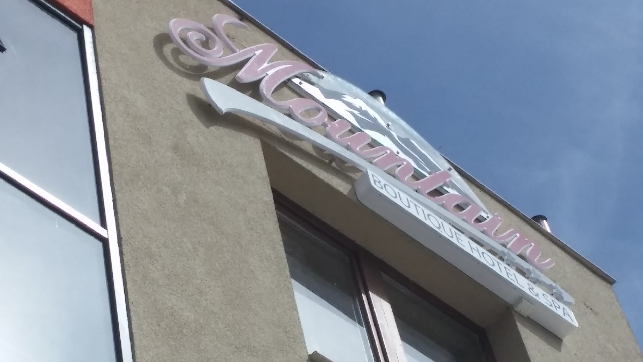 Табела на хотел, заснета от нисък ъгъл, показваща розов надпис "Mountain" и бял елемент с текст "Boutique Hotel & Spa".