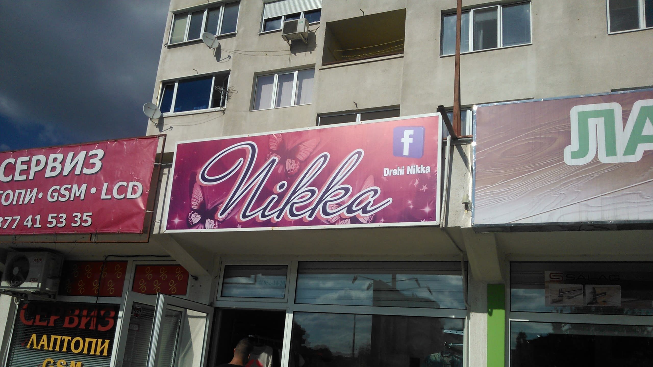 Розова табела на магазин, монтирана на фасада на сграда, на фона на облачно небе и съседни рекламни пана.