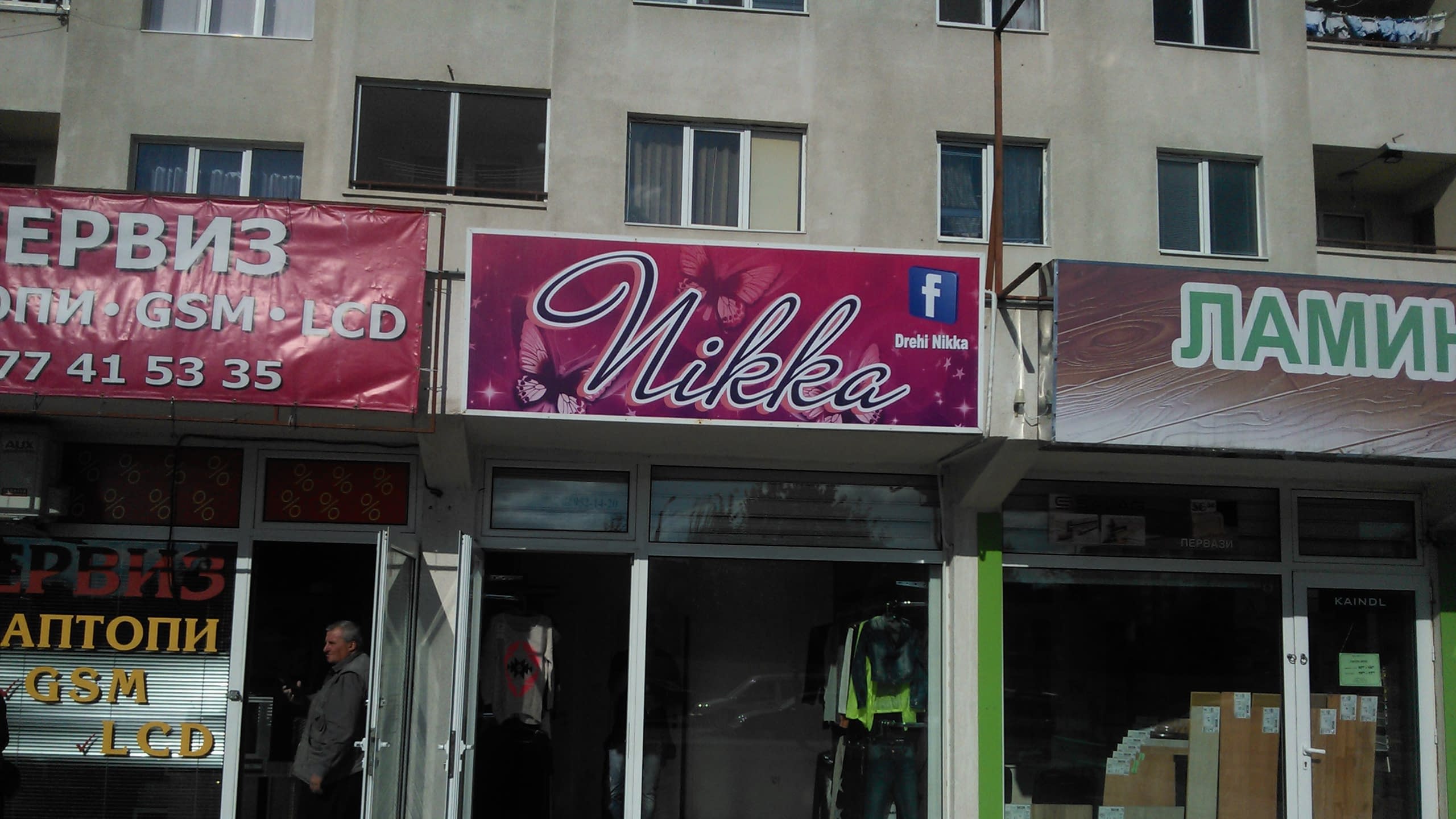 Изглед към входовете на два съседни магазина, единият с розова табела "Nikka", другият с червена табела "Сервиз".
