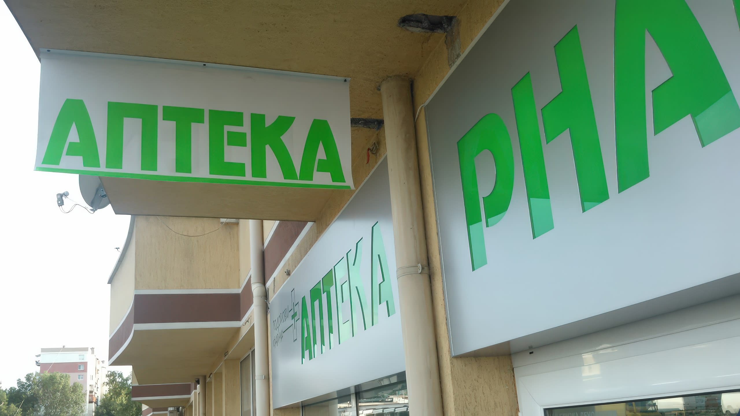 Табели на аптека, заснети отдолу, показващи издаден напред надпис "Аптека" и други надписи на фасадата.