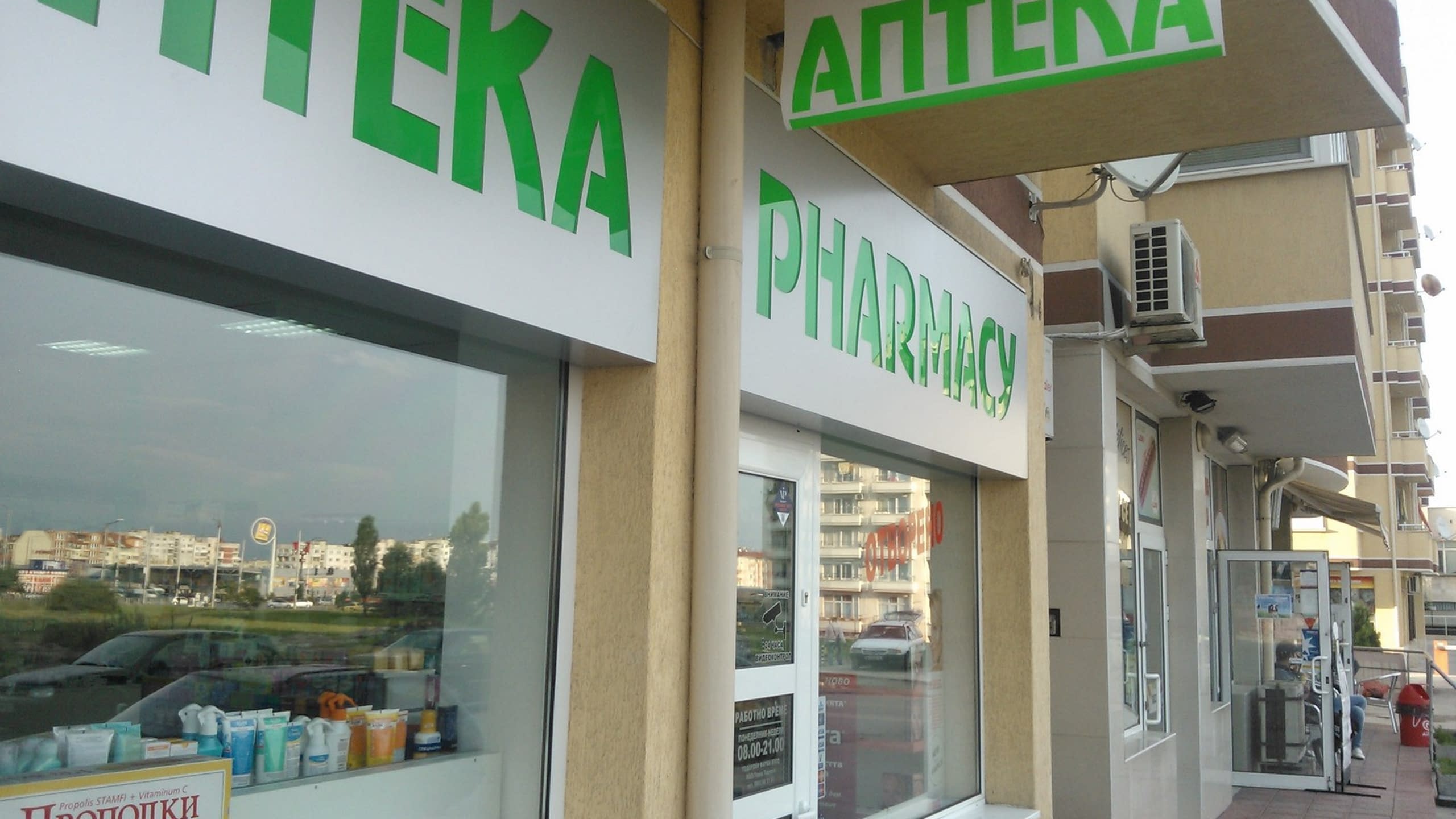 Изглед към ъгъла на аптека с няколко табели със зелени надписи "Аптека" и "Pharmacy" на български и английски език.