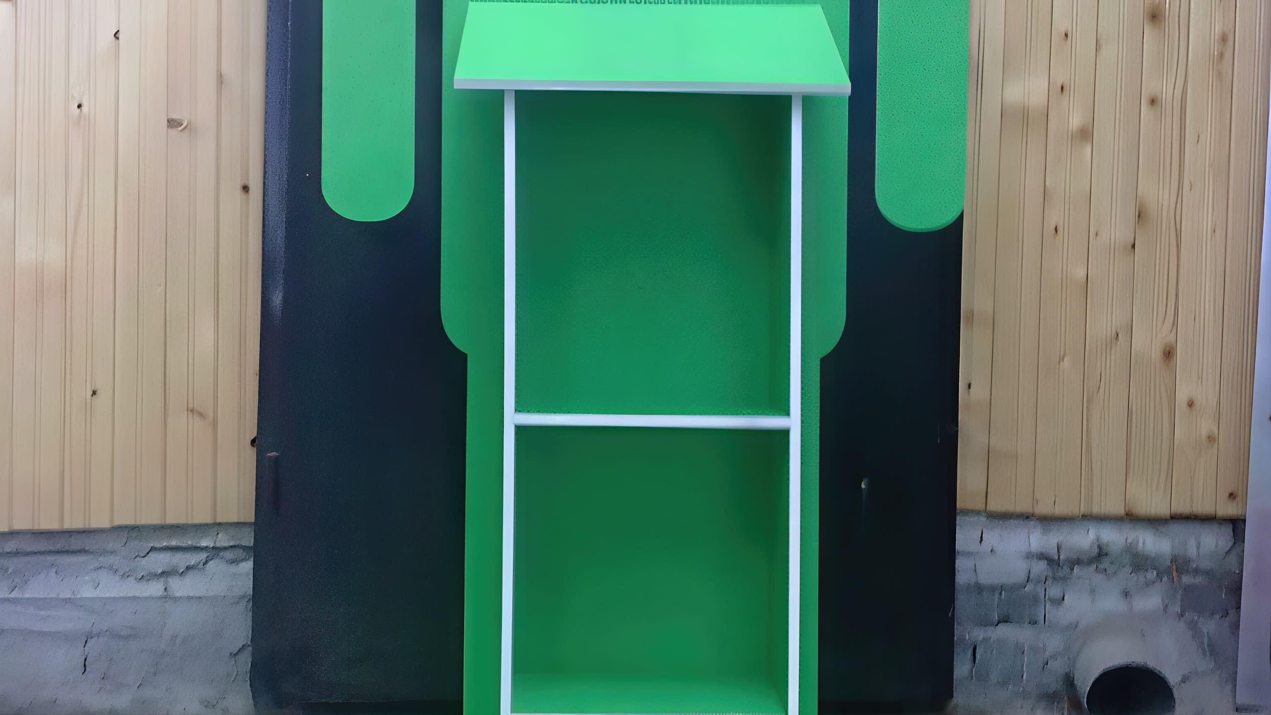 Задната част на зелен и черен стелаж, поставен до стена с дървена ламперия.