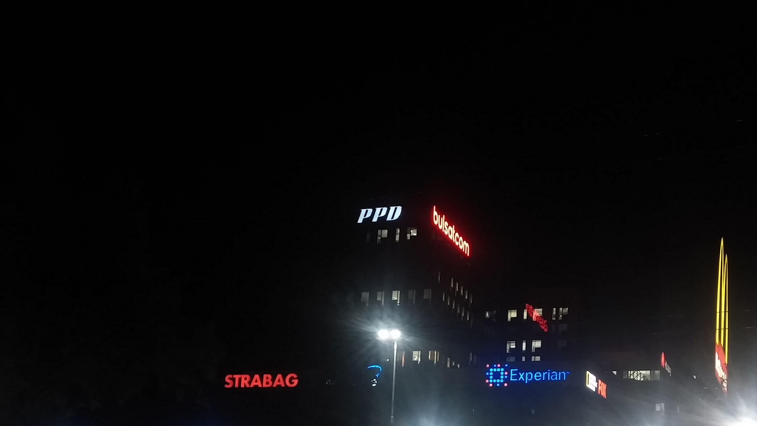 Нощна снимка на няколко светещи фирмени надписа върху сгради, сред които PPD, Bulsatcom и Experian.