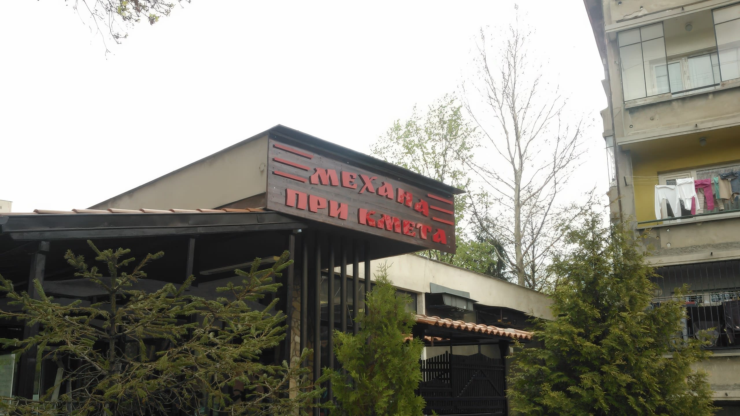 Табела с червени обемни букви "Механа При Кмета" на дървена основа, монтирана на сграда.