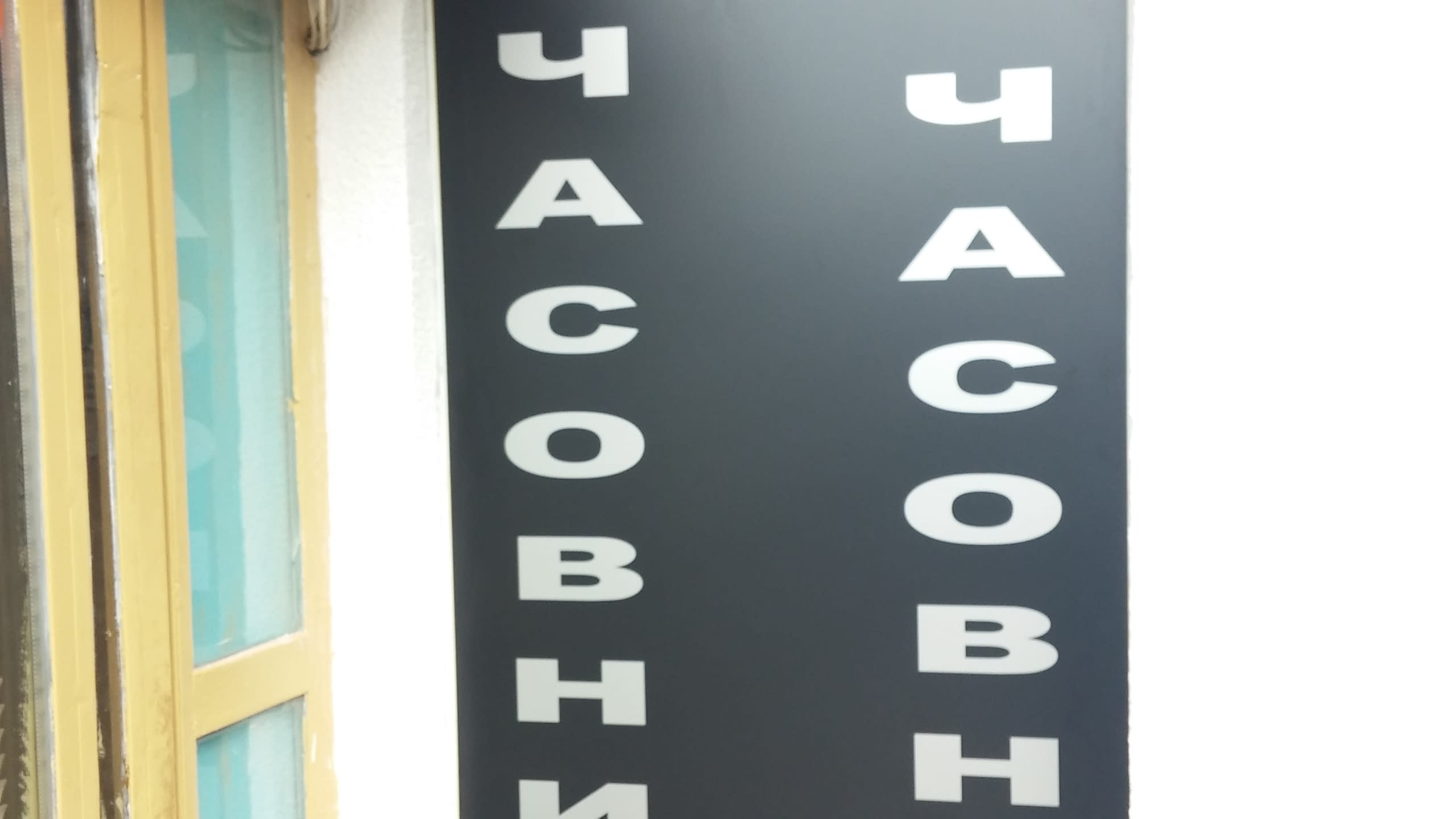 Близък план на вертикален надпис "Часовникар" с бели букви на черна табела.