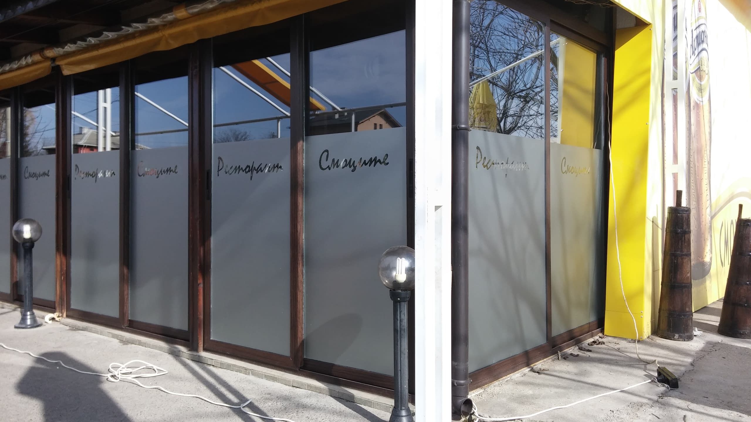 Ъглов изглед на ресторант с матирано фолио на прозорците и жълта тента.