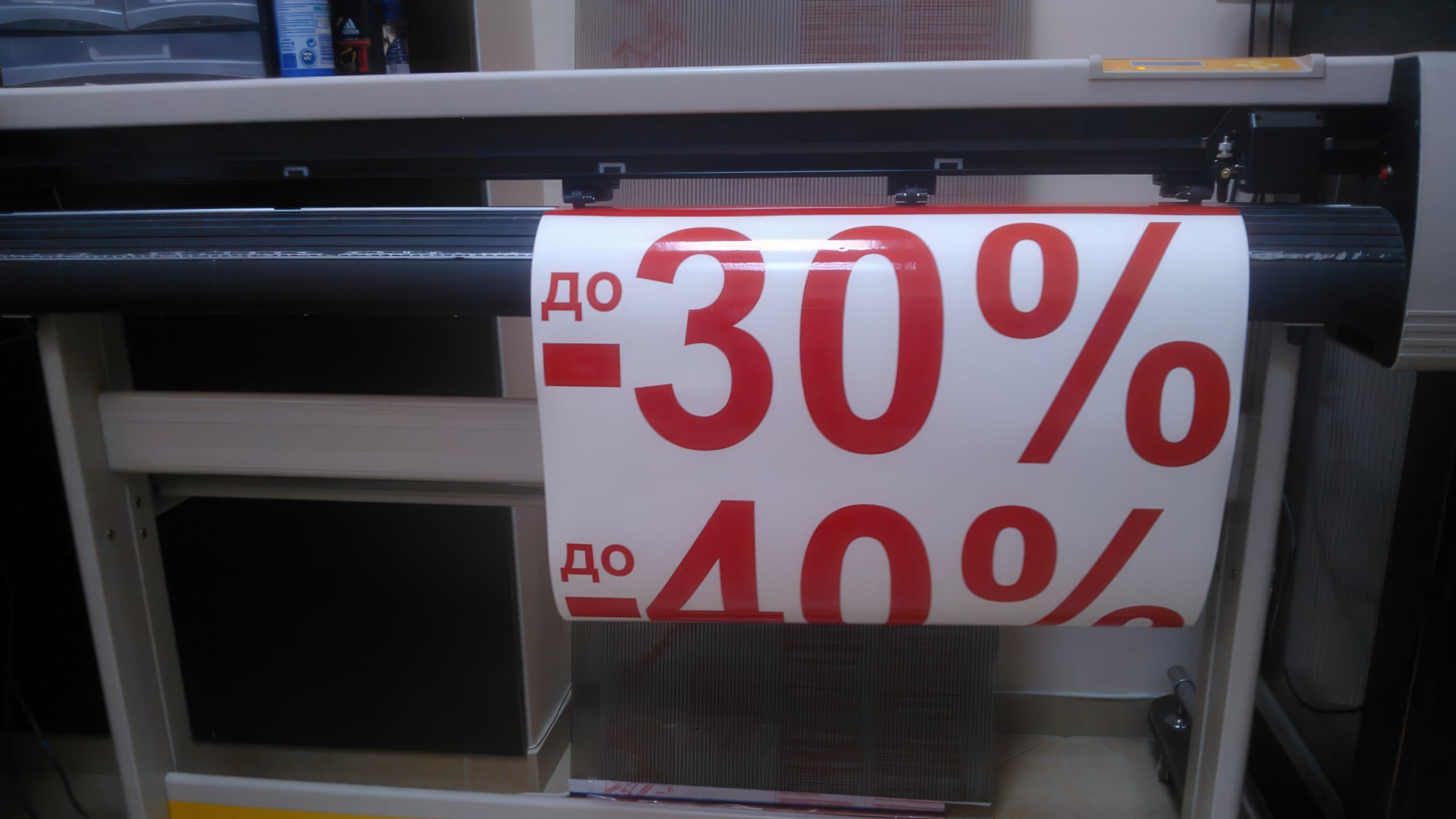 Близък план на метален режещ инструмент, който се движи по повърхността на бял лист и очертава контура на червения надпис „ДО -30%“.