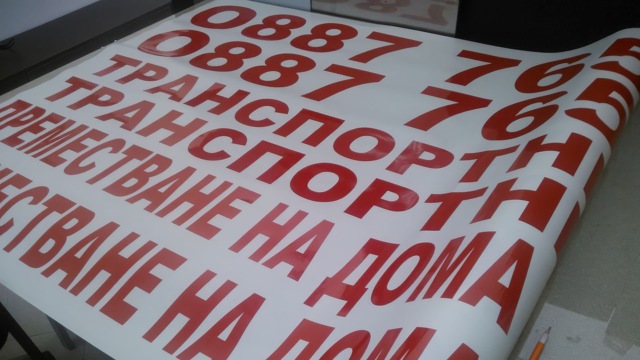 Близък план на лист с червени самозалепващи се букви, образуващи думи като „ТРАНСПОРТ“ и „ПРЕМЕСТВАНЕ НА ДОМА“.