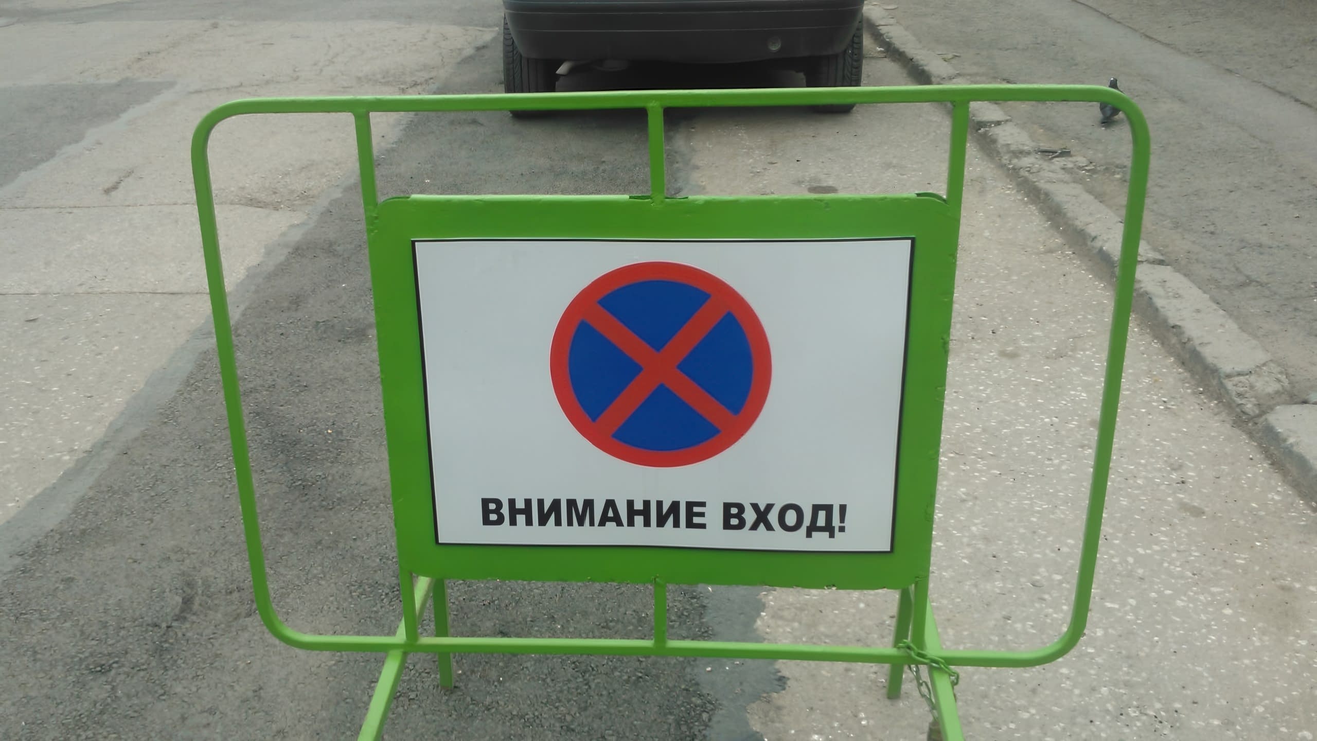 Подвижна зелена преграда със забранителна табела за паркиране, поставена на улицата пред вход.