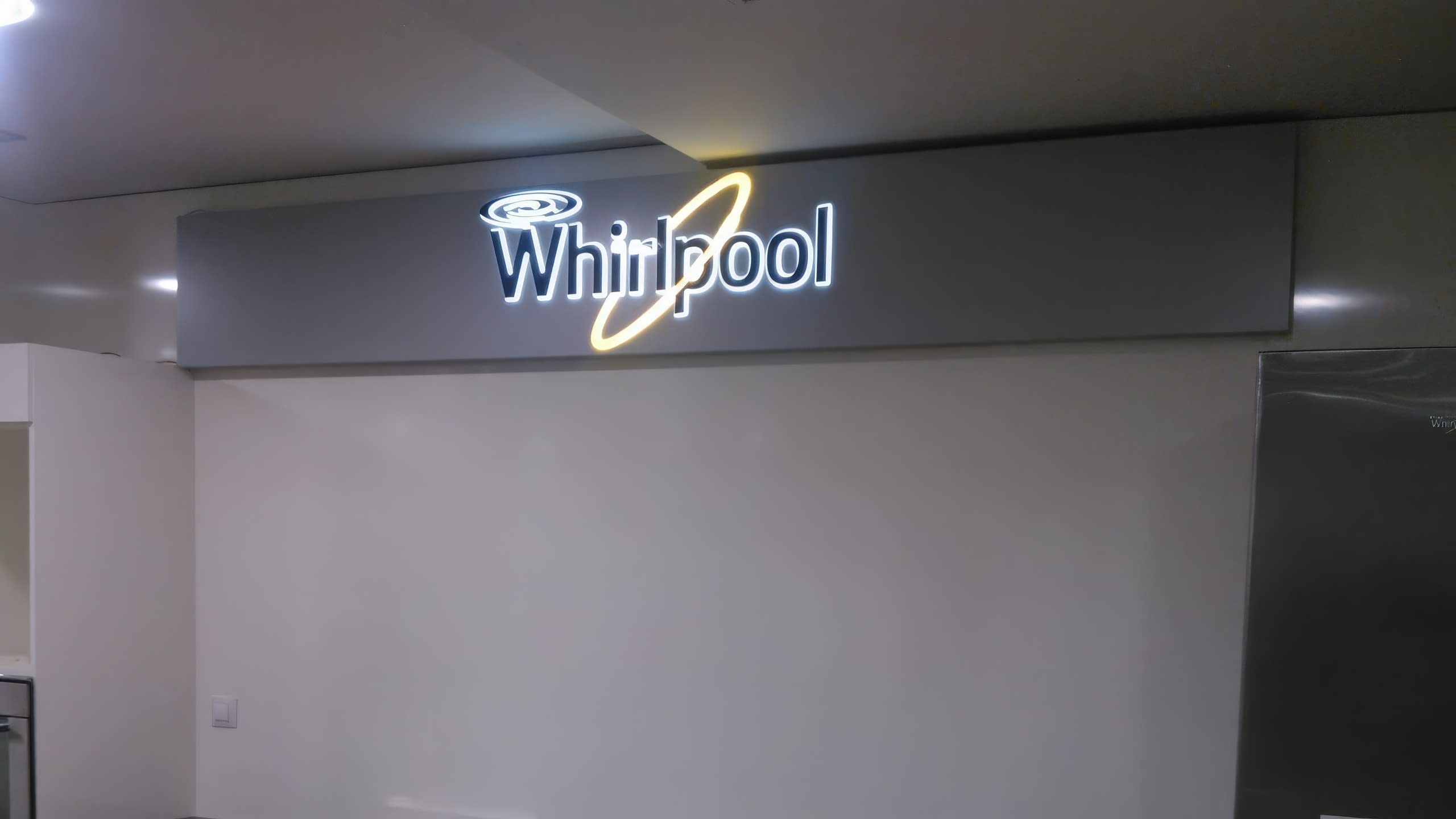 Изложбен щанд за домакински уреди със светещо лого на Whirlpool на стената.