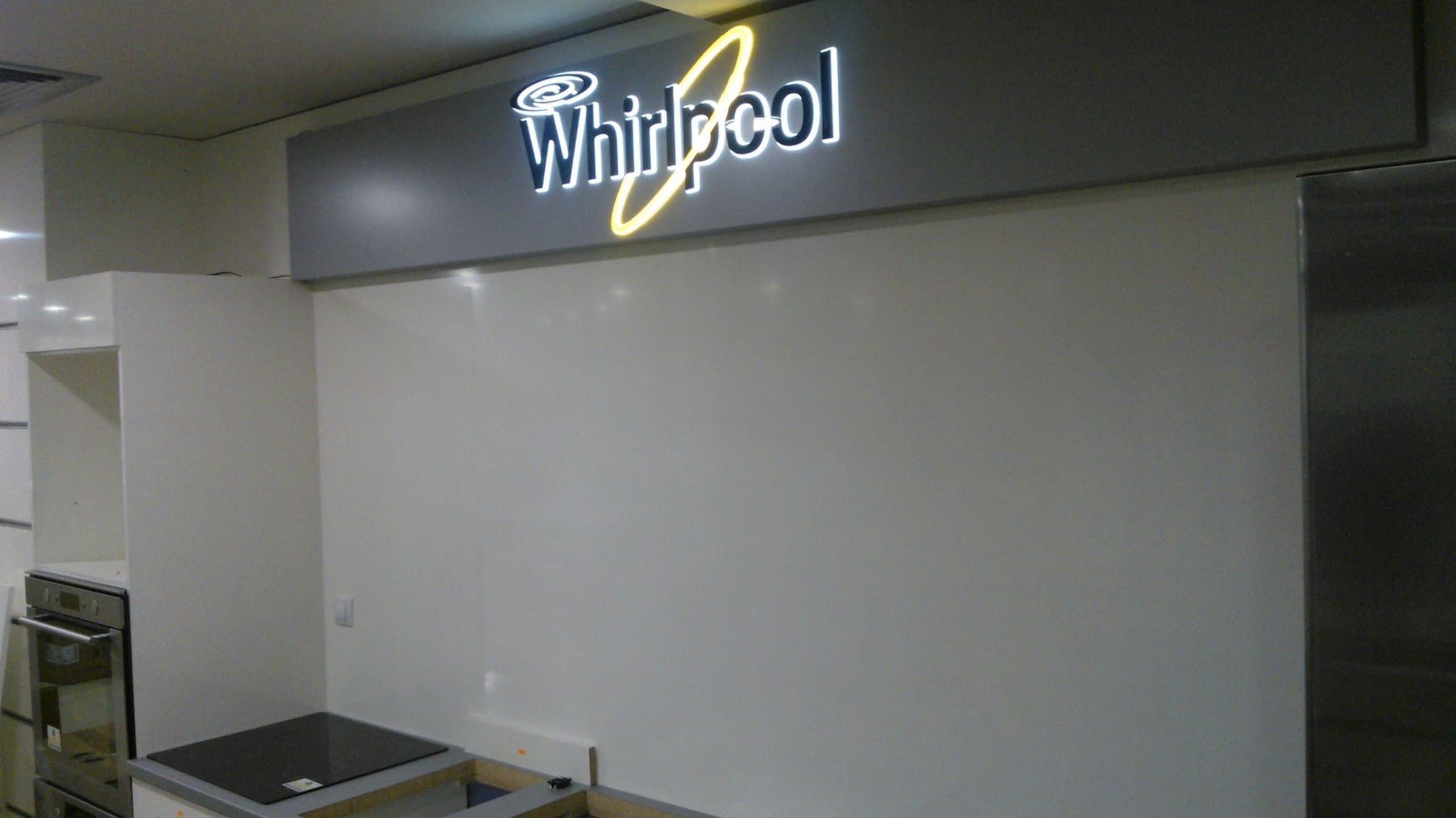 Дълга правоъгълна светеща табела с лого на Whirlpool, монтирана на стена в интериор.