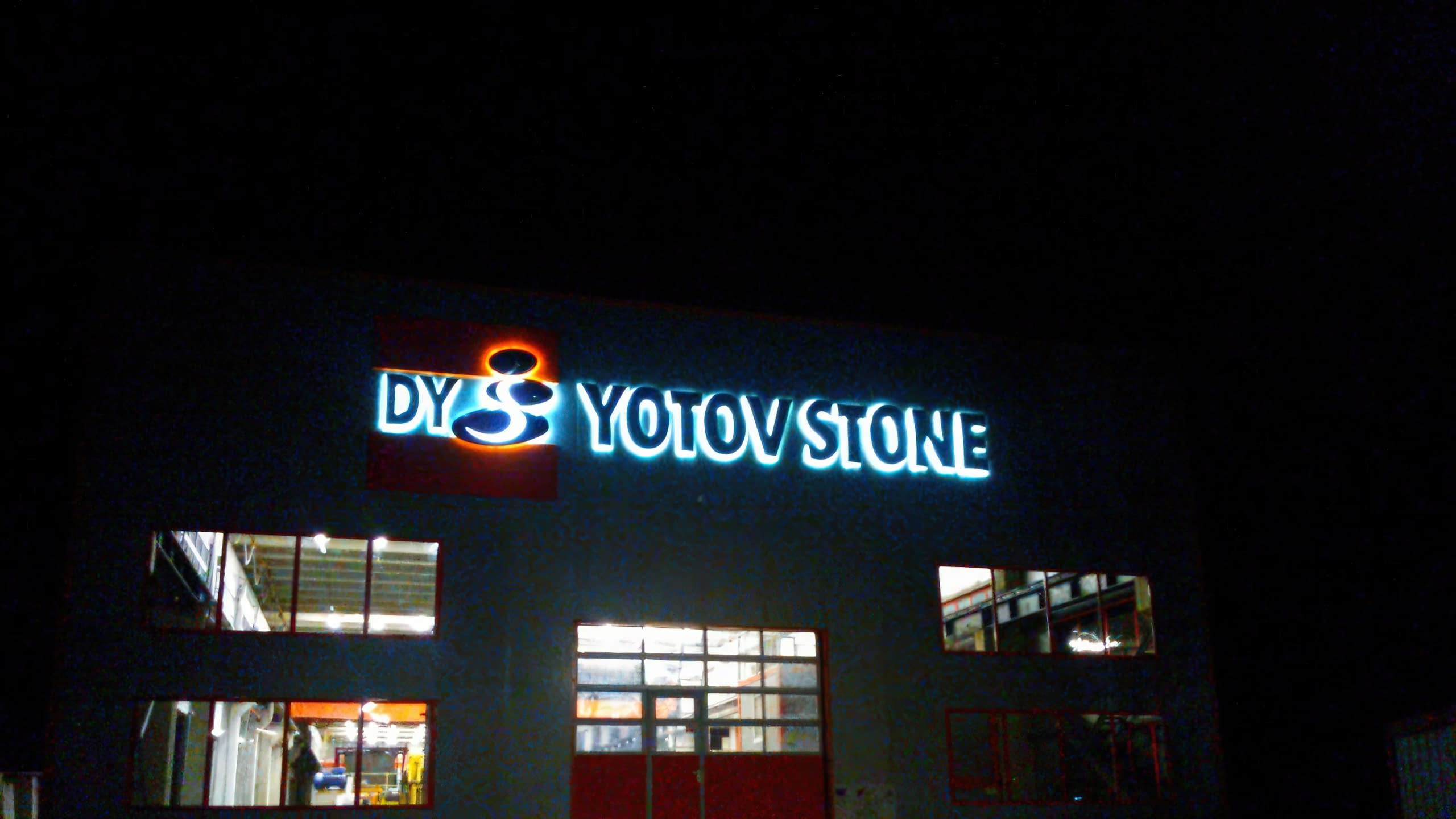 Светещ в бяло и оранжево фирмен надпис на голяма сграда през нощта.