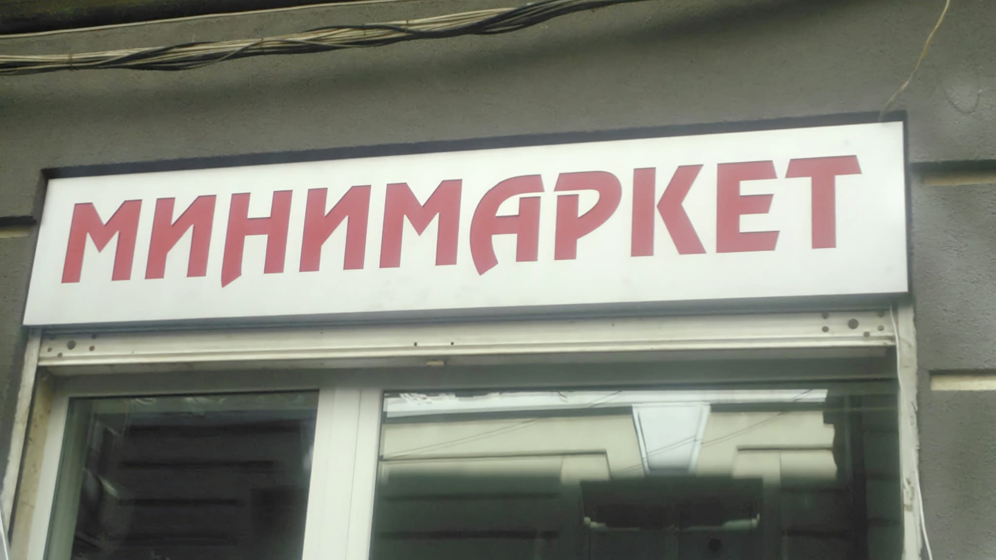 Светеща реклама за минимаркет – табела с червени букви „Минимаркет“ върху бял фон, монтирана над витрината на магазин.