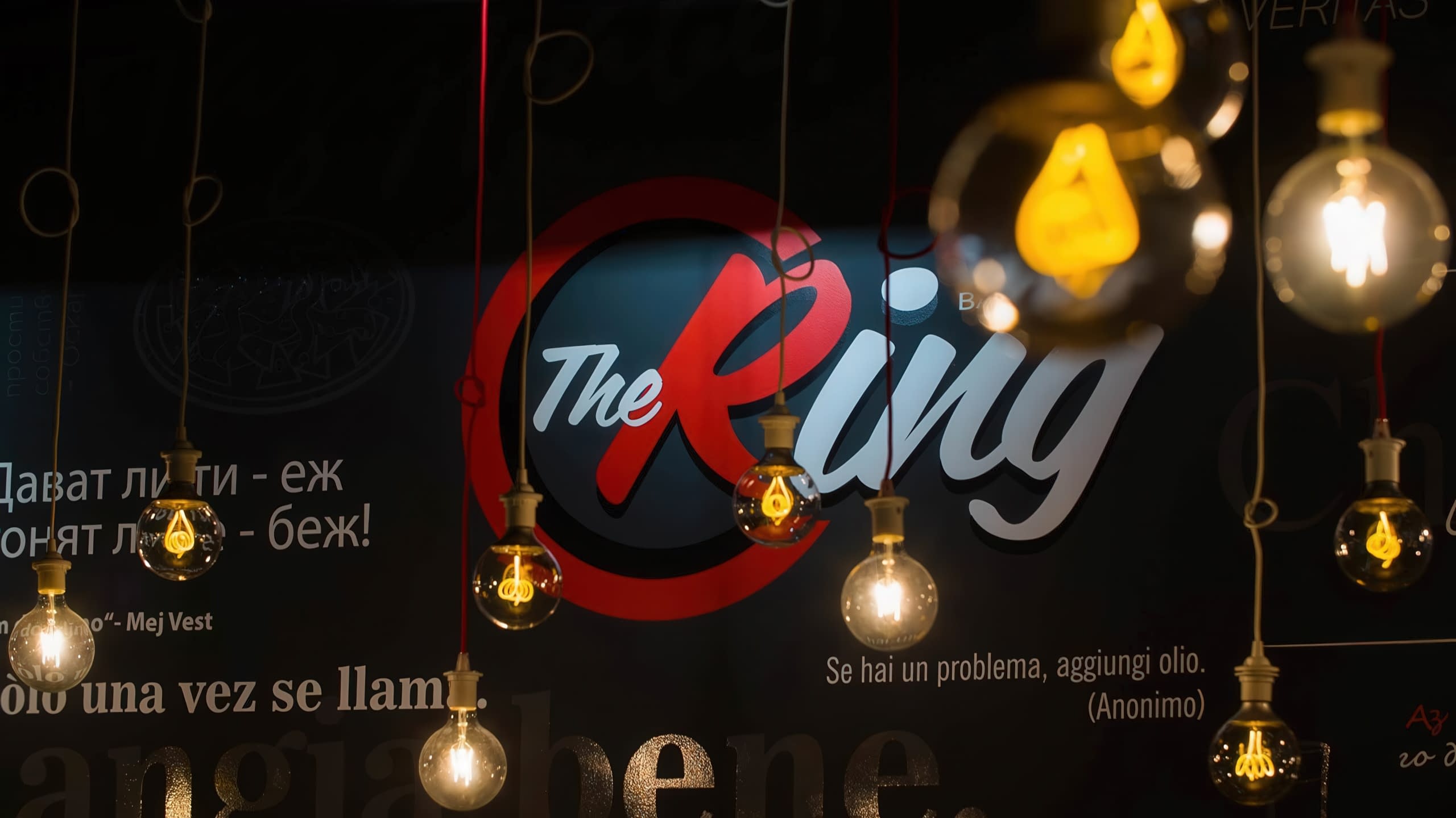 Интериор на ресторант с лого на стената "The Ring" и декоративни ретро крушки, създаващи уютна атмосфера.