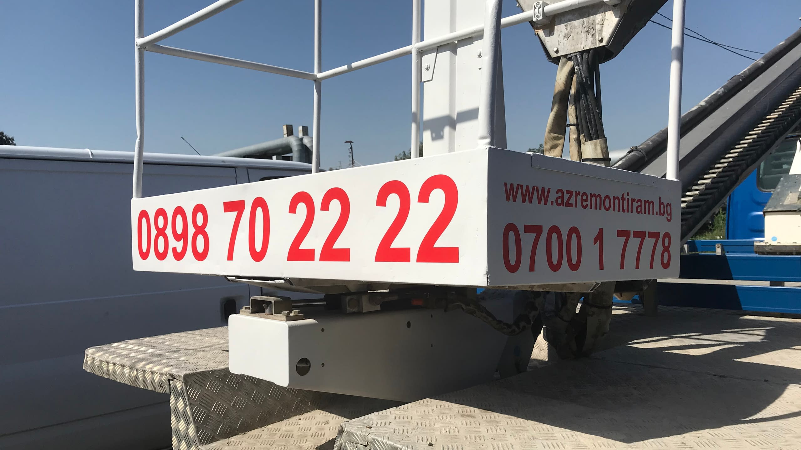 Рекламен надпис от червено фолио върху бяла работна платформа на вишка. Ясно изписани телефони за връзка и уебсайт на фирма "azremontiram.bg".