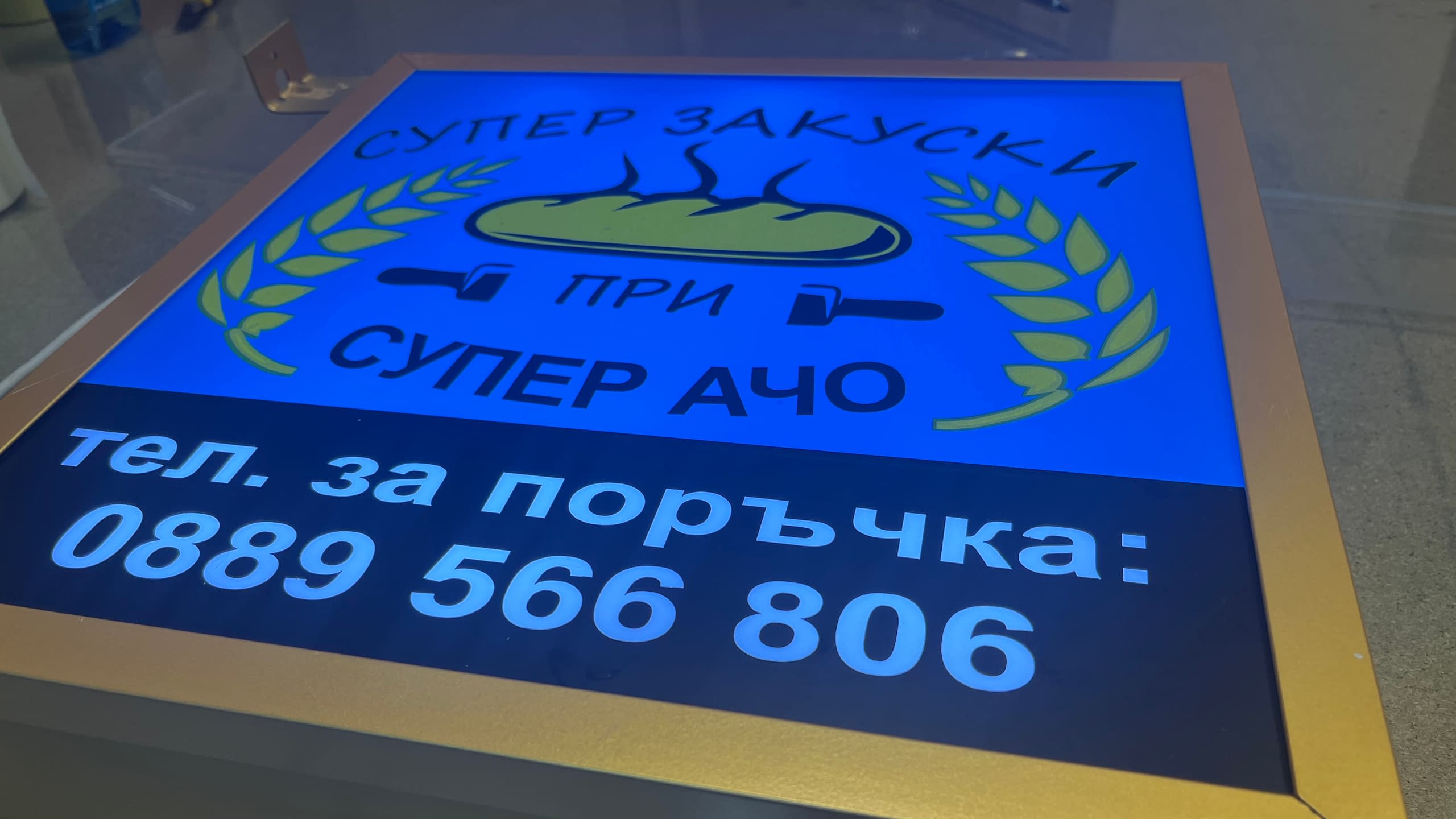 Правоъгълна светеща табела (лайтбокс) за закусвалня "Супер Закуски при Супер Ачо". Синя рекламна табела със светещи надписи, лого и телефон за поръчки.