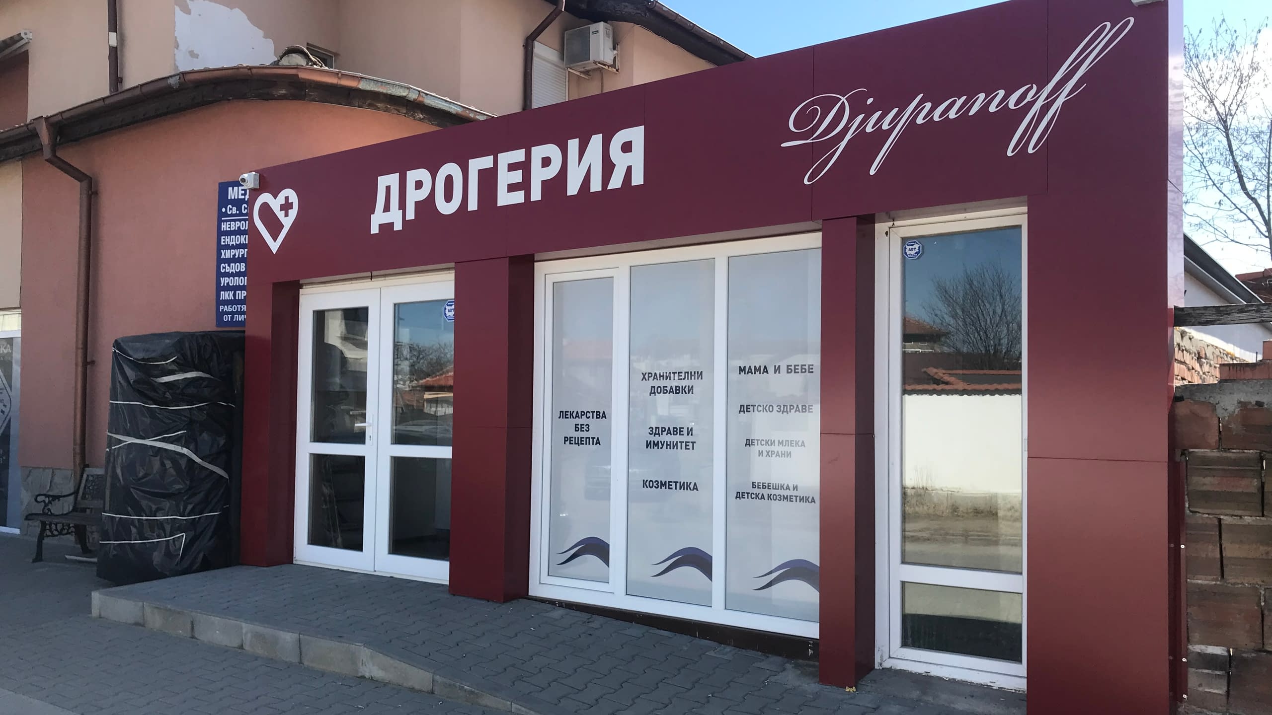 Цялостно брандиране на дрогерия "Djuranoff" с голяма рекламна табела и надписи от бяло фолио върху витрините, изброяващи категории продукти. Професионална външна реклама.