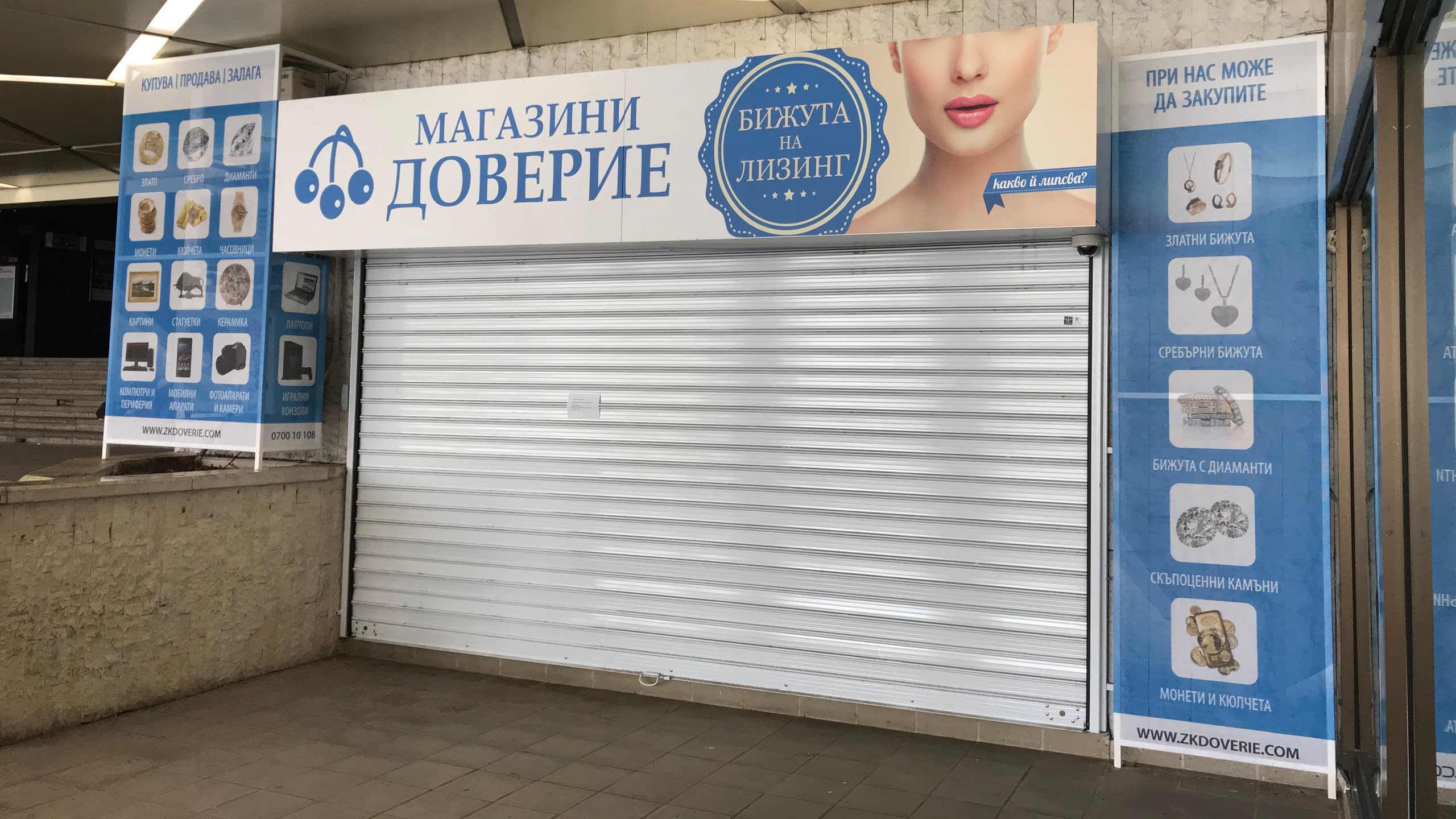 Вход на "Магазини Доверие", брандиран с рекламни винили, показващи предлаганите стоки и услуги.