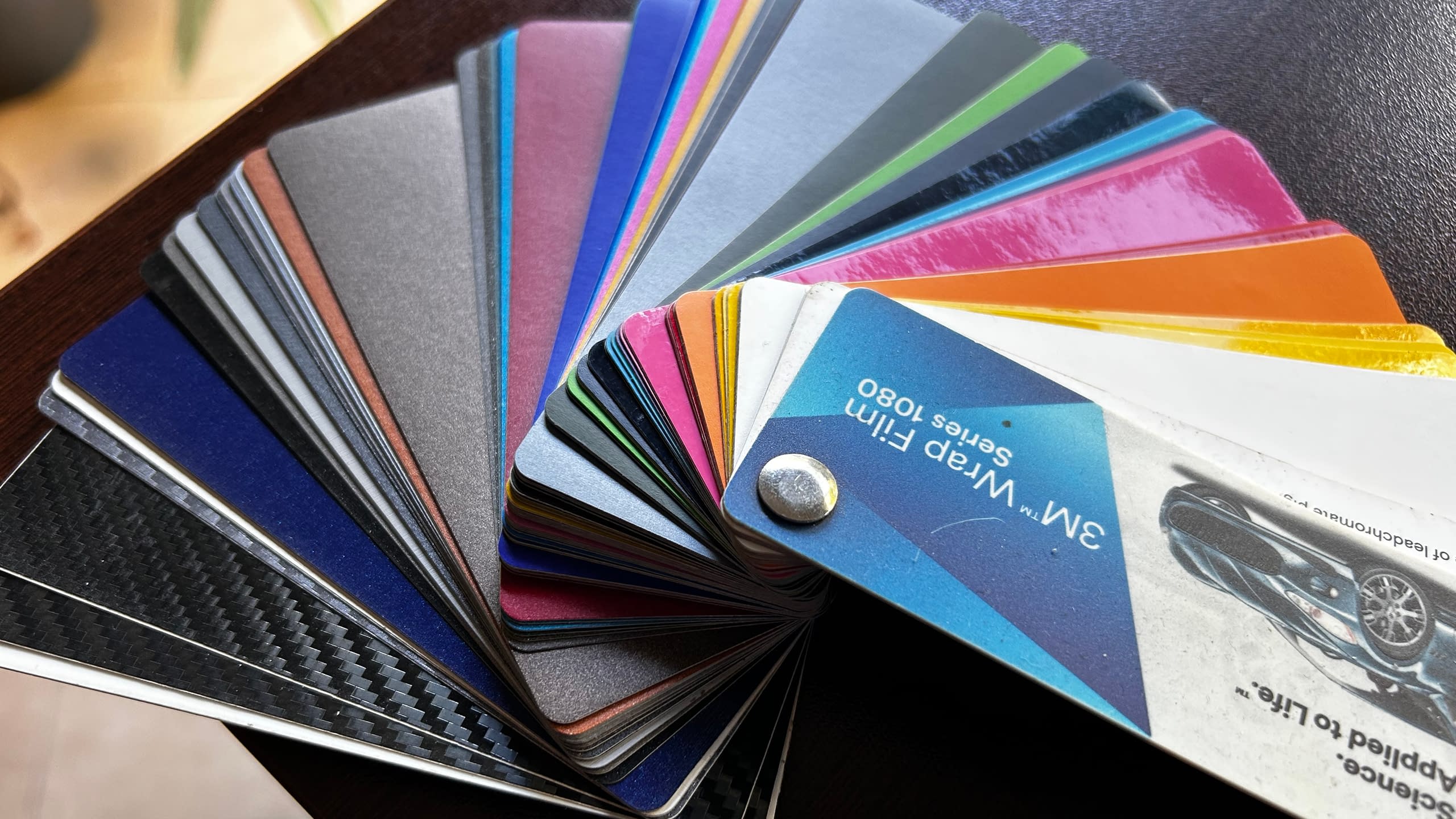 Цветови каталог с мостри на автомобилно фолио "3M™ Wrap Film Series 1080", показващ различни цветове и текстури, включително карбон и мат.