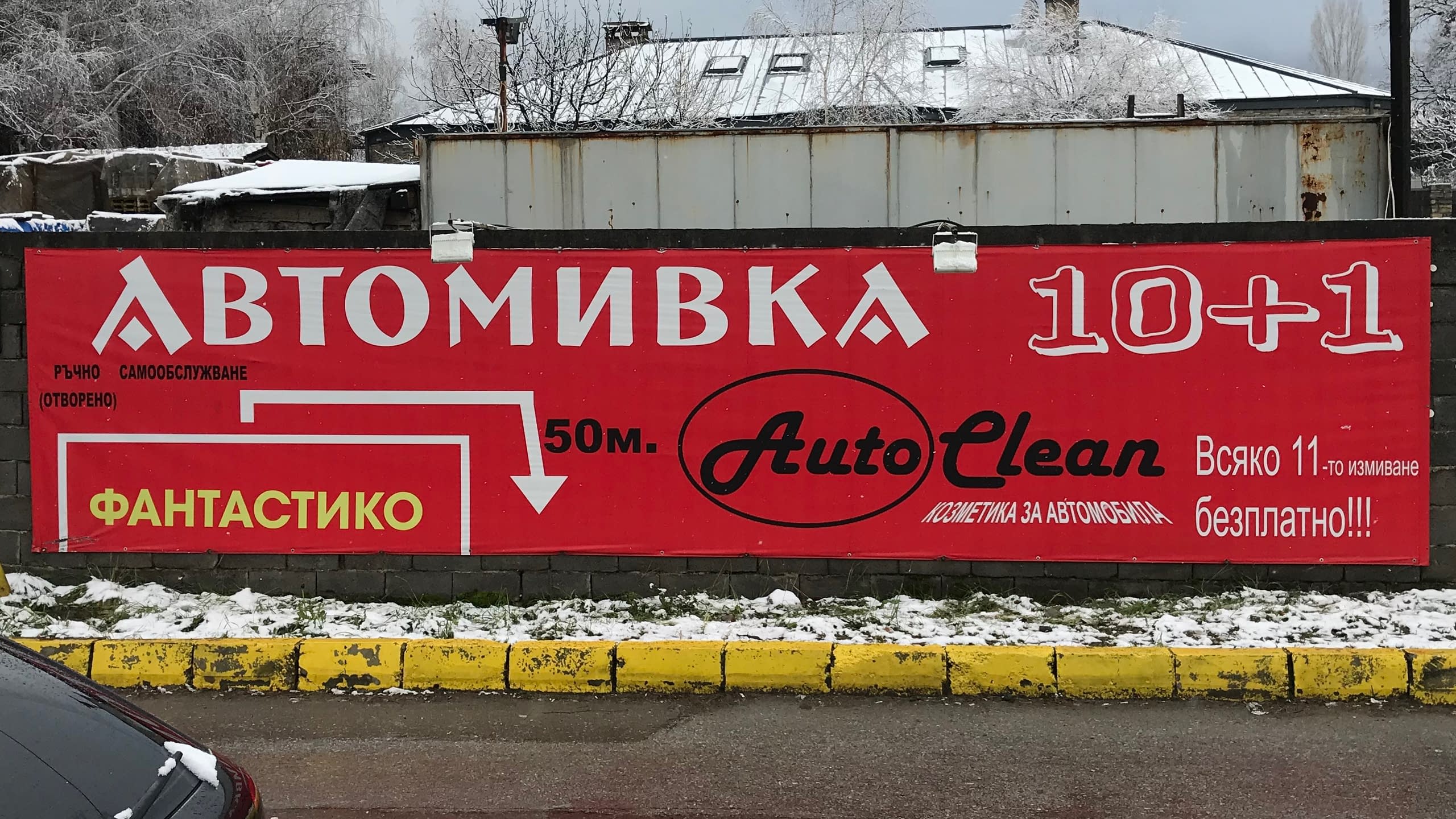 Рекламно платно за автомивка "Auto Clean" с промоционална оферта 10+1. Червен банер, монтиран на ограда, с информация за услугите и местоположението.