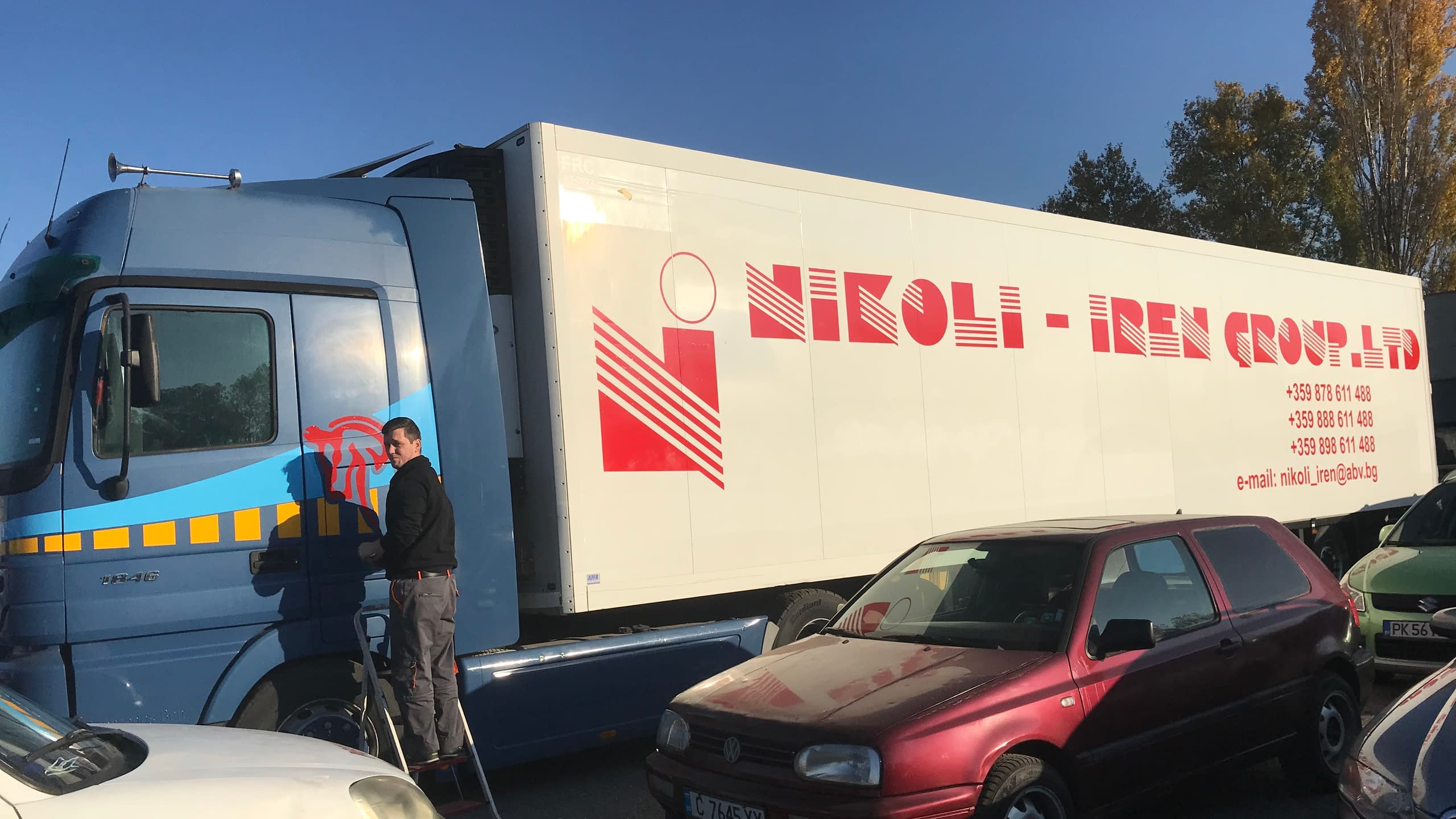 Процес по брандиране на бяло ремарке на камион с лого и контакти на фирма "NIKOLI - IREN GROUP LTD", изрязани от червено фолио.