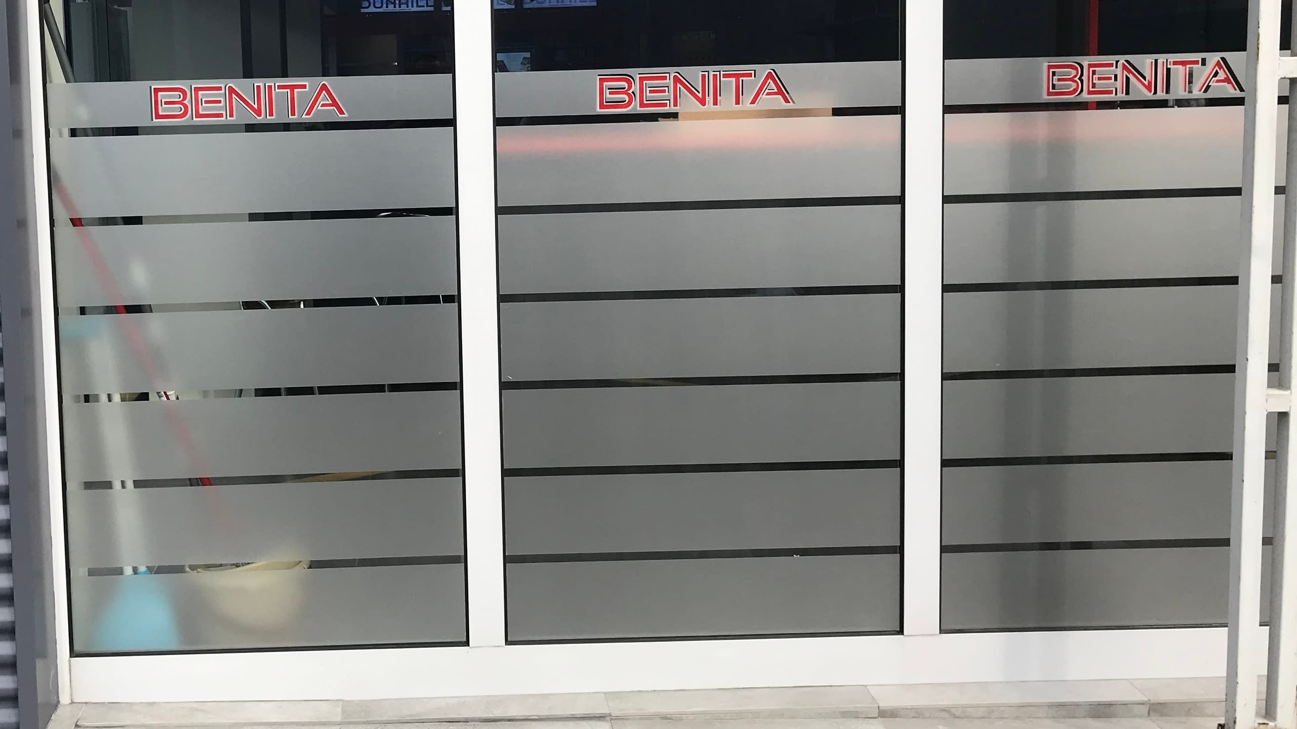 Брандирана стъклена витрина на магазин "BENITA" с матирано (пясъкоструйно) фолио на ленти и червени изрязани надписи.
