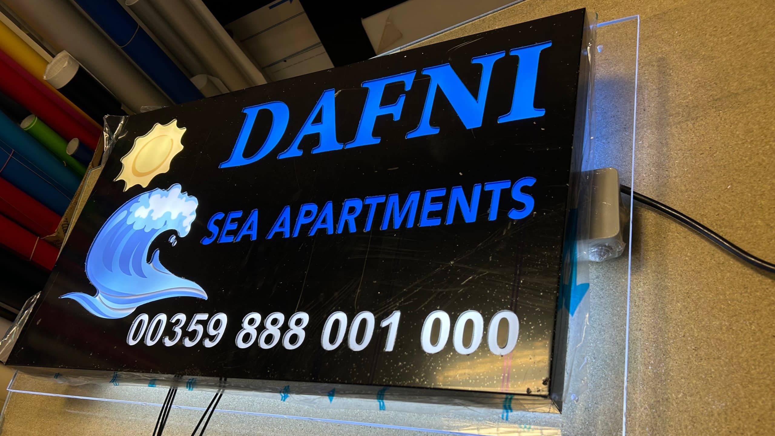 Светеща табела в процес на изработка за хотел "DAFNI SEA APARTMENTS" с пълноцветно лого, надписи и телефонен номер.
