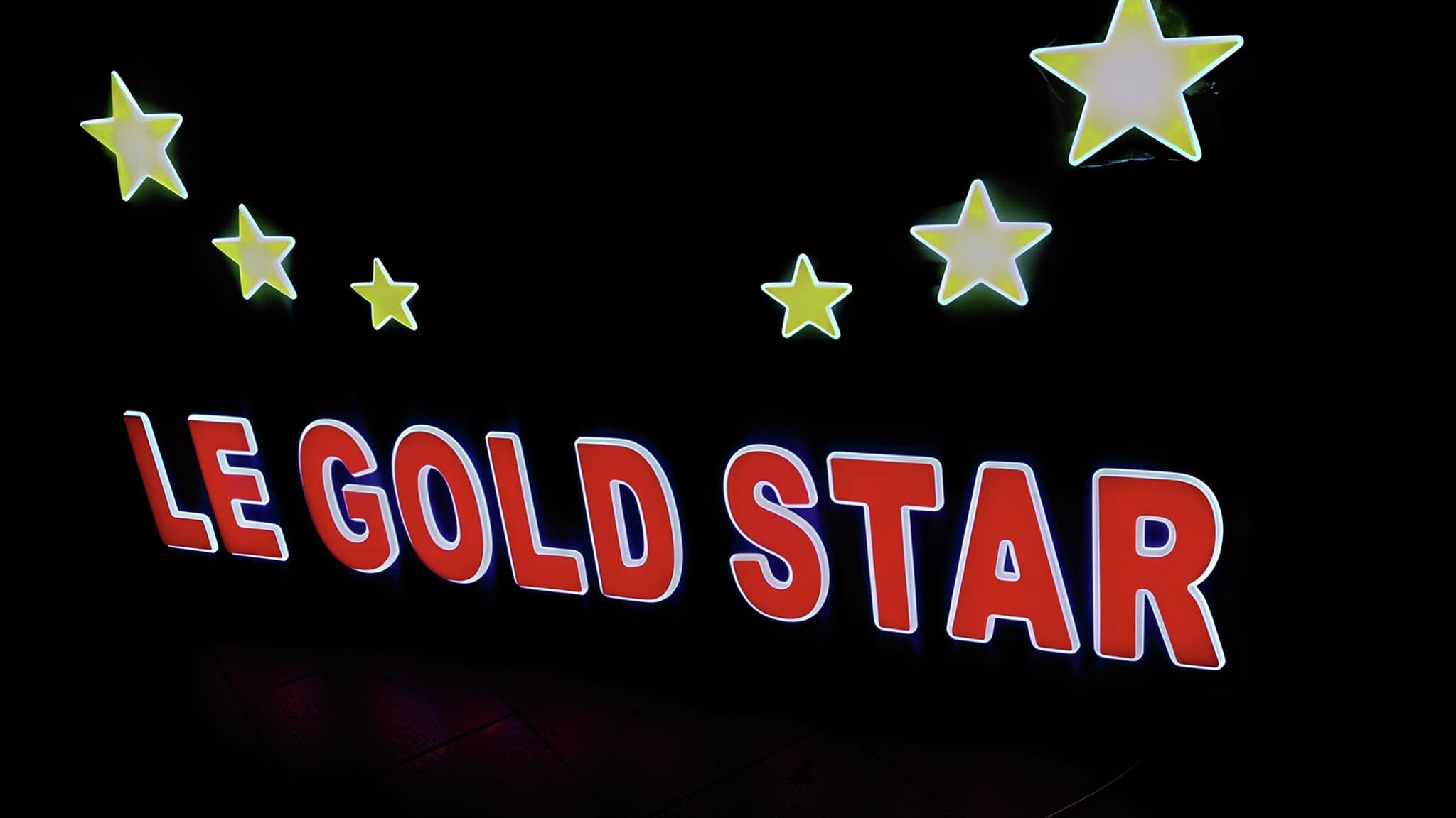 Светеща рекламна табела 'Le Gold Star' с червени букви и жълти звезди – подходяща за нощни заведения.
