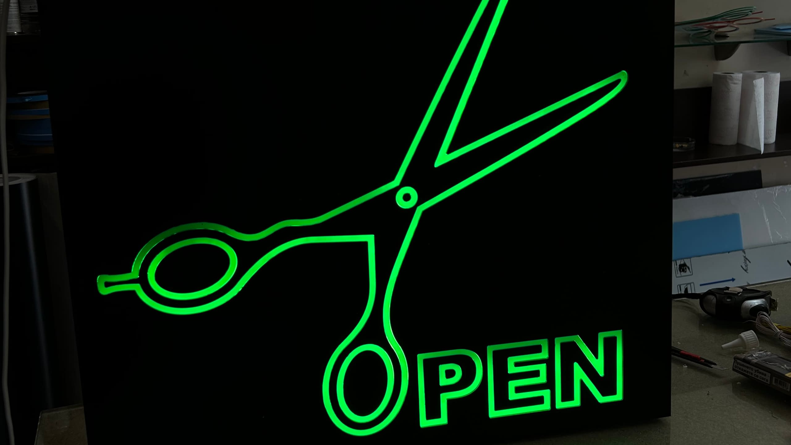 Квадратна светеща табела "OPEN" със зелено светещо гравирано изображение на ножица, подходяща за фризьорски салон.