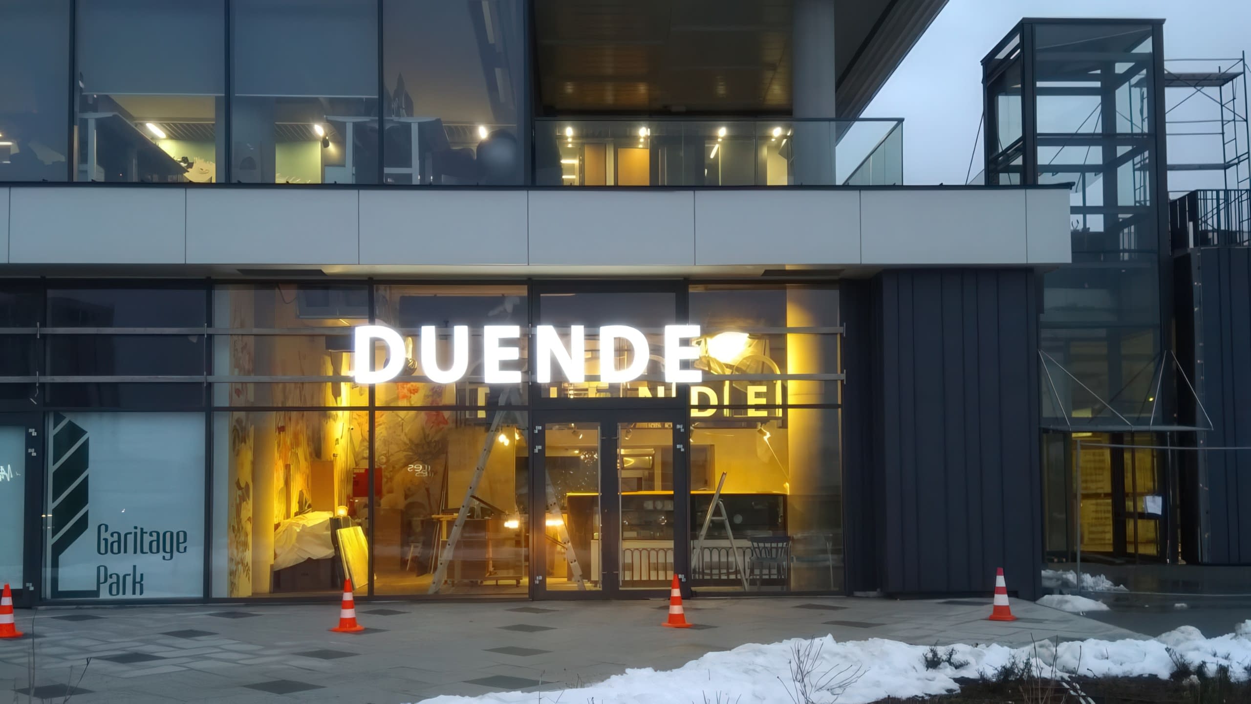Светещи обемни букви с надпис "DUENDE", монтирани на стъклена фасада на модерна сграда в Гаритаж Парк.