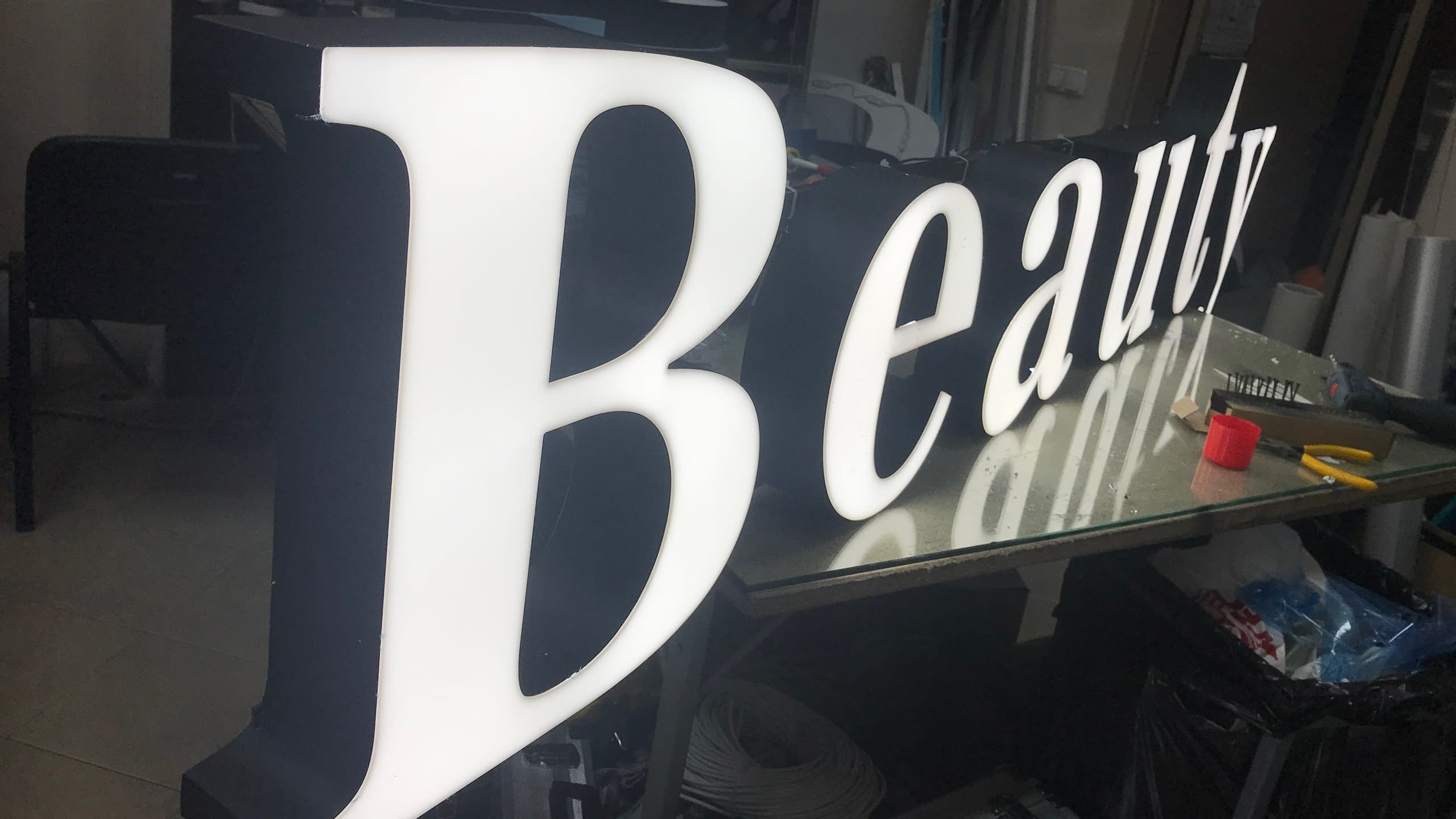 Големи бели светещи обемни букви с надпис "Beauty" в процес на изработка в рекламно ателие.