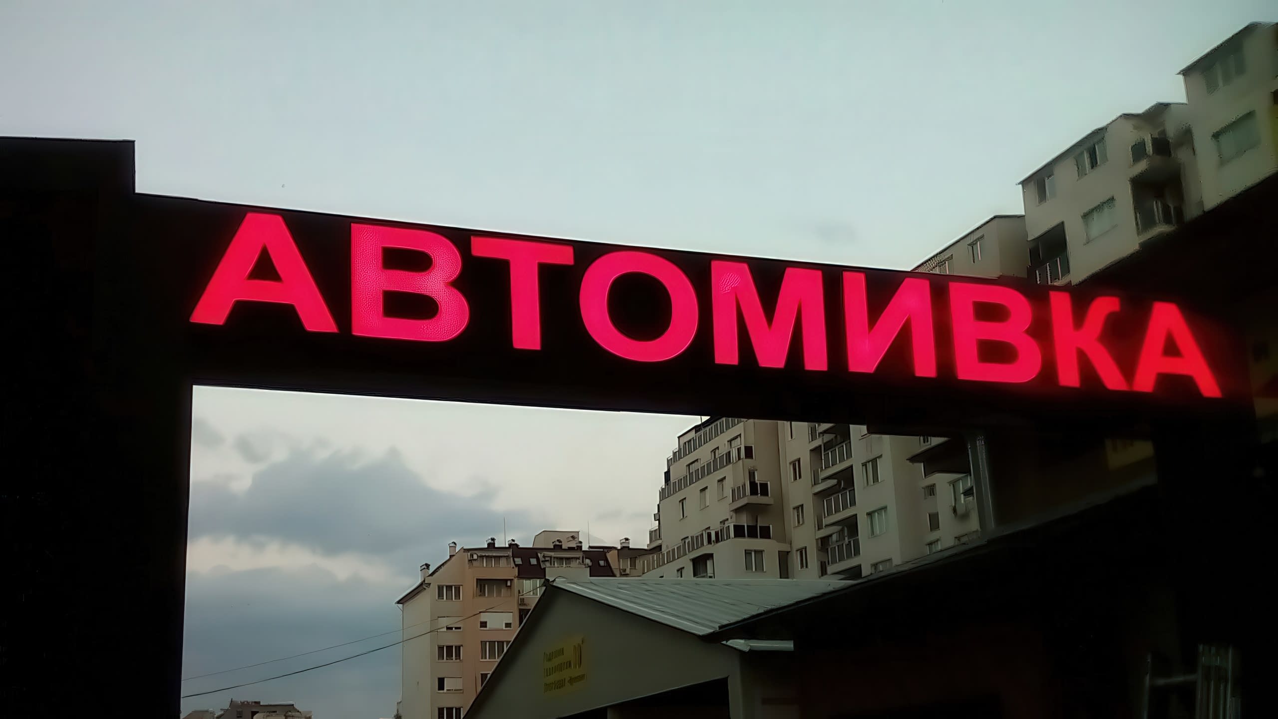 Голяма външна светлинна реклама с яркочервен светещ надпис "АВТОМИВКА", монтирана на тъмна основа.