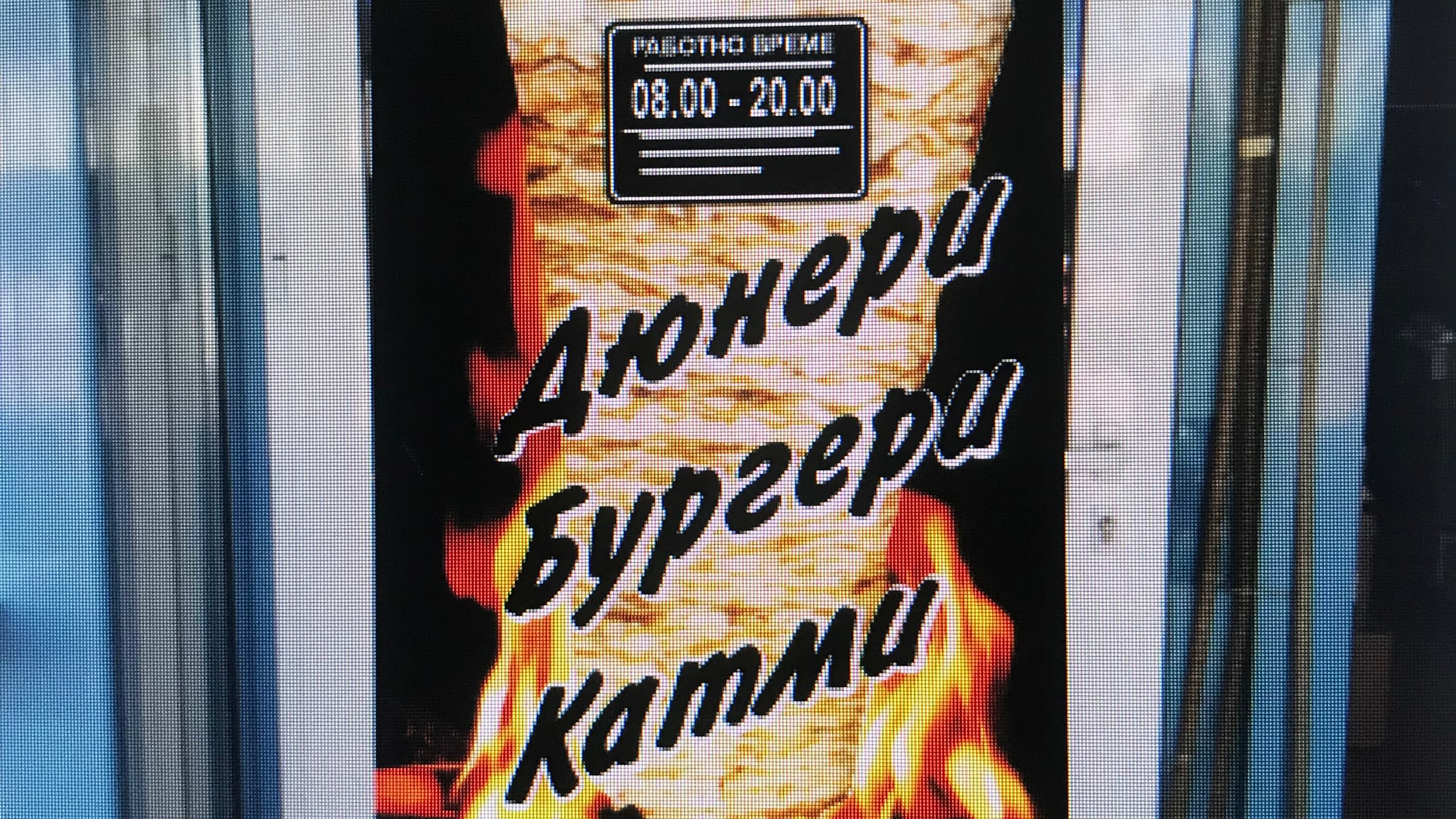 Светеща рекламна табела за заведение за бързо хранене с надписи "Дюнери Бургери Катми" на апетитен фон с пламъци.