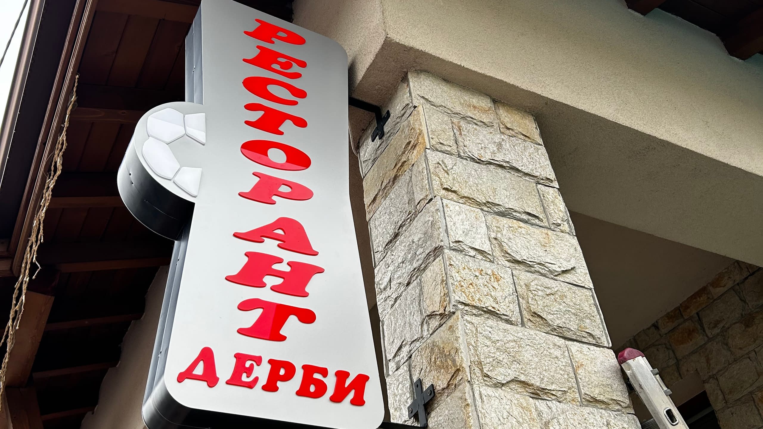 Вертикална двустранна конзолна табела за "Ресторант ДЕРБИ" с червени обемни букви и релефна футболна топка.