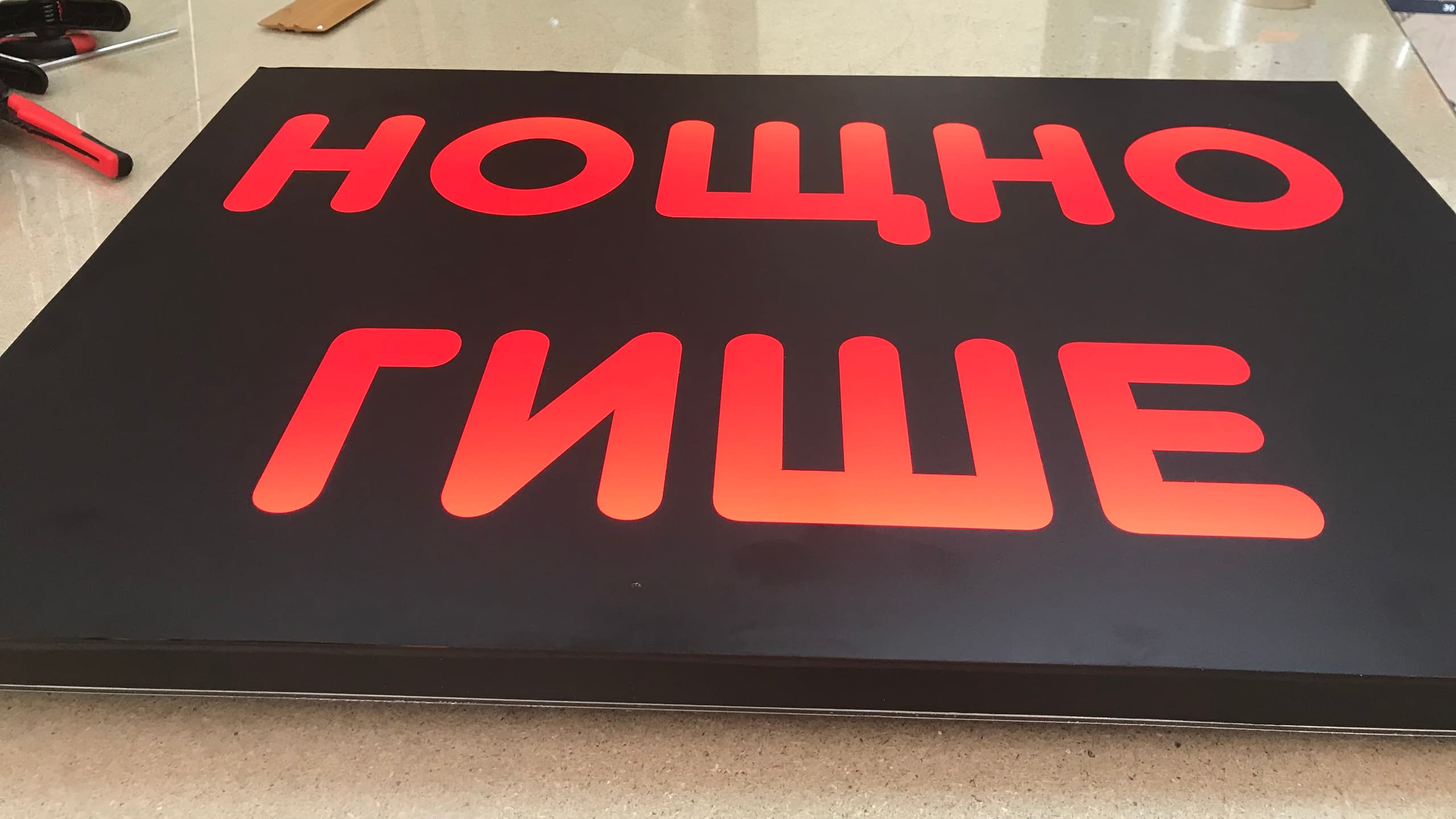 Светеща правоъгълна табела с черен фон и яркочервен надпис "НОЩНО ГИШЕ", подходяща за денонощно заведение.