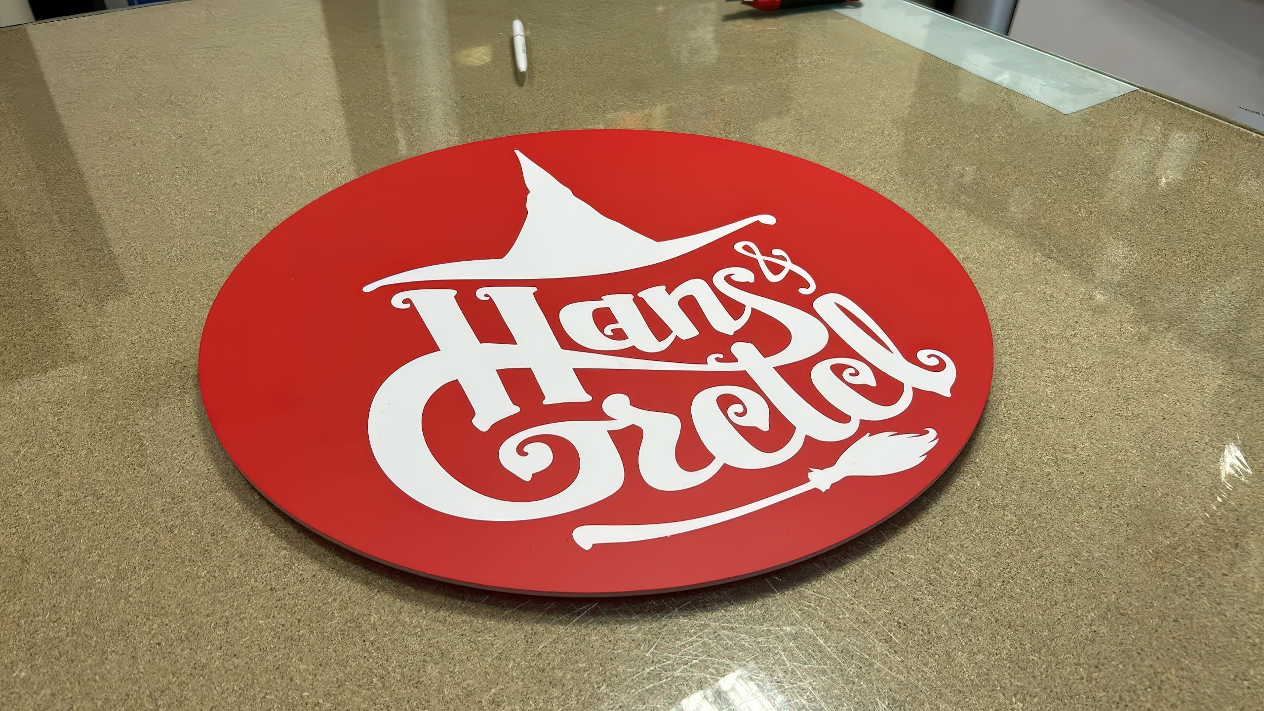 Кръгла червена рекламна табела с бяло приказно лого за заведение "Hans & Gretel", заснета в процес на изработка.
