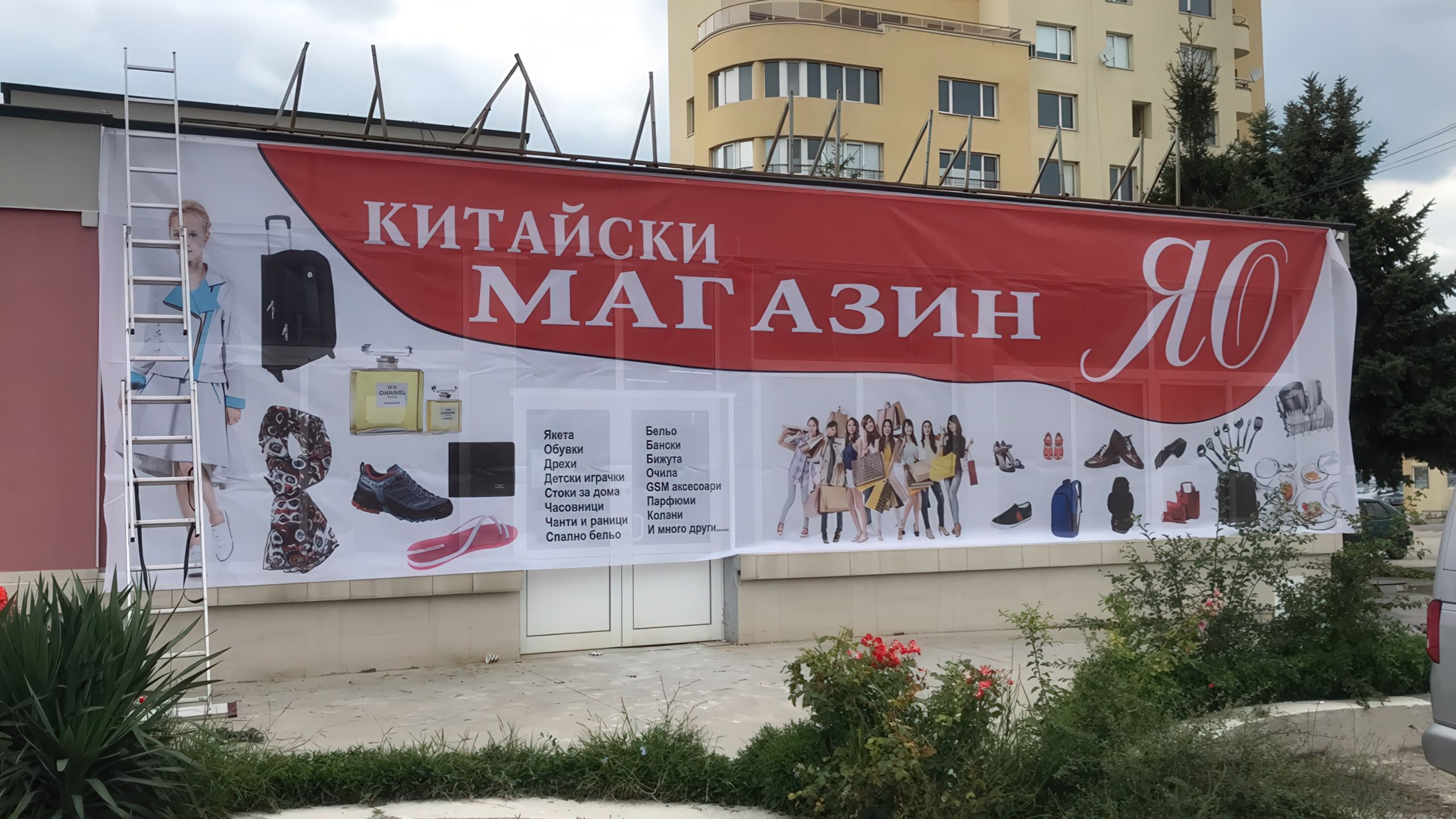 Голям рекламен транспарант от винил на фасадата на "Китайски магазин ЯО" с описание на предлаганите стоки.